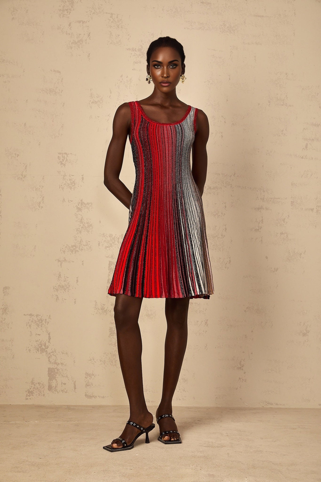 A woman wearing a red mini dress with horizontal sequin stripes and long sleeves standing against a plain background