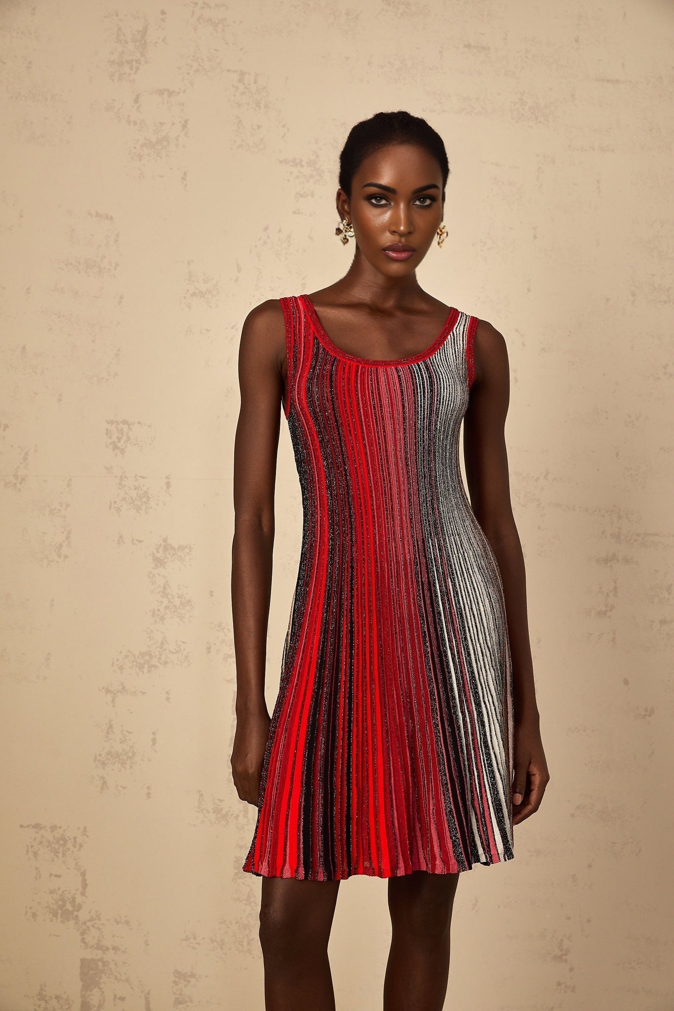 A woman wearing a red mini dress with horizontal sequin stripes knitted into the fabric The dress has a form fitting silhouette and ends above the knee