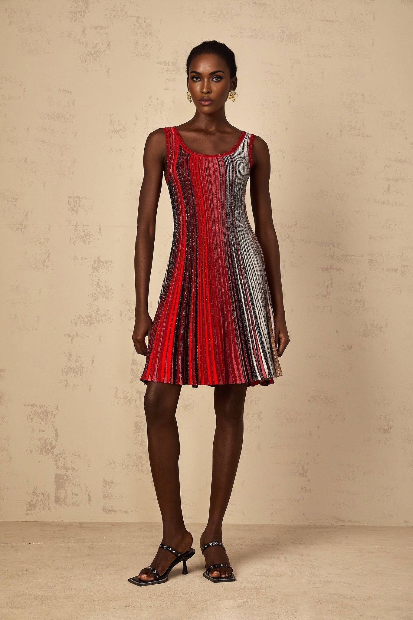 A woman wearing a red mini dress with horizontal sequin stripes standing against a plain background