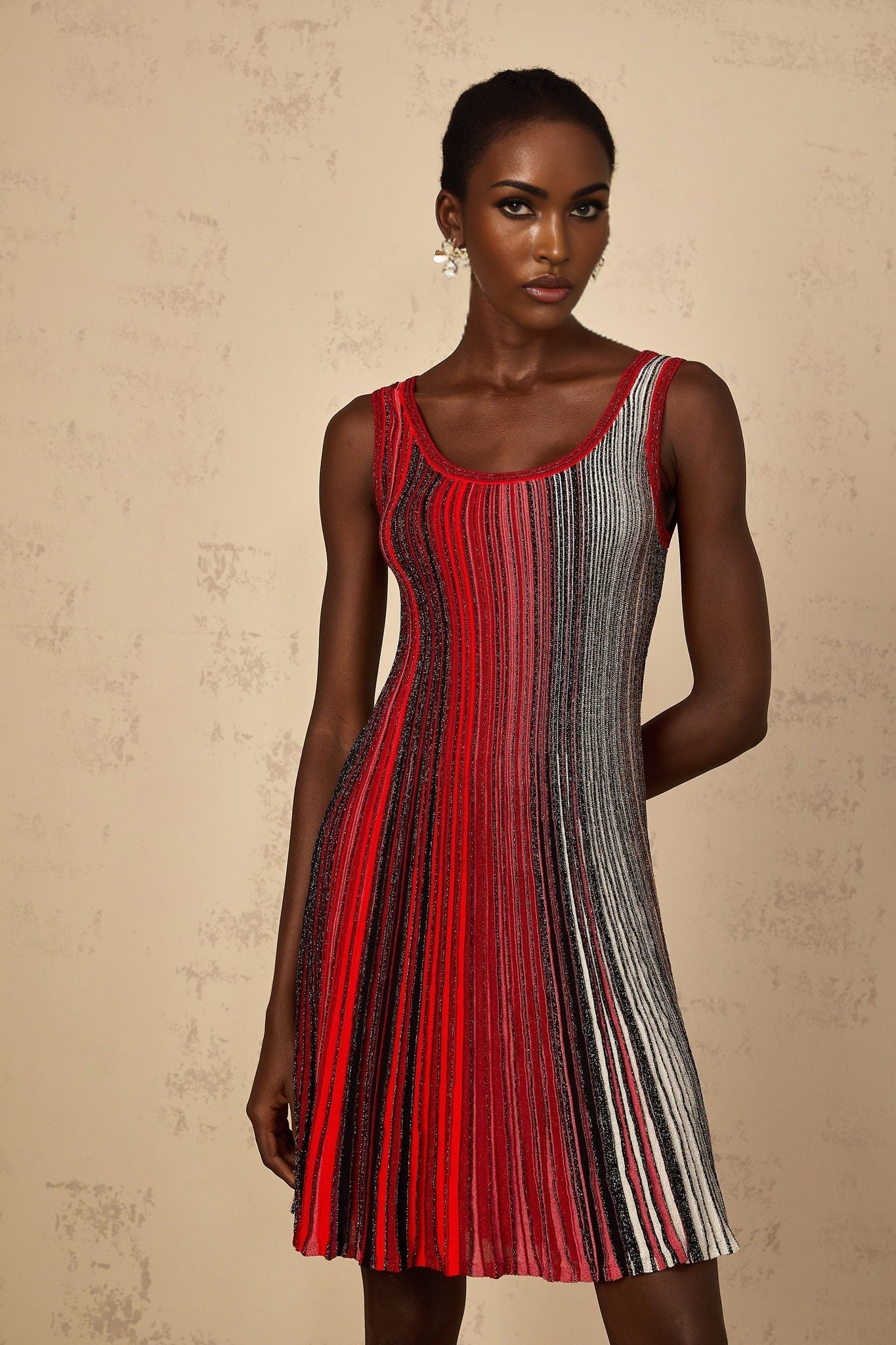 A woman wearing a red mini dress with sequin stripes and a knit fabric standing in a neutral pose