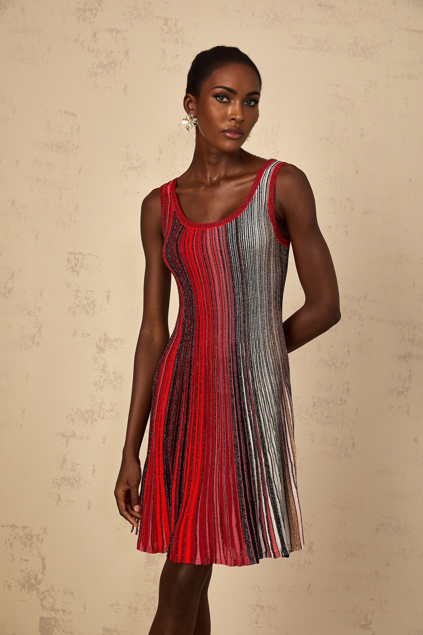 A woman wearing a red mini dress with sequin stripes knitted into the fabric The dress has a form fitting silhouette and reaches above the knees