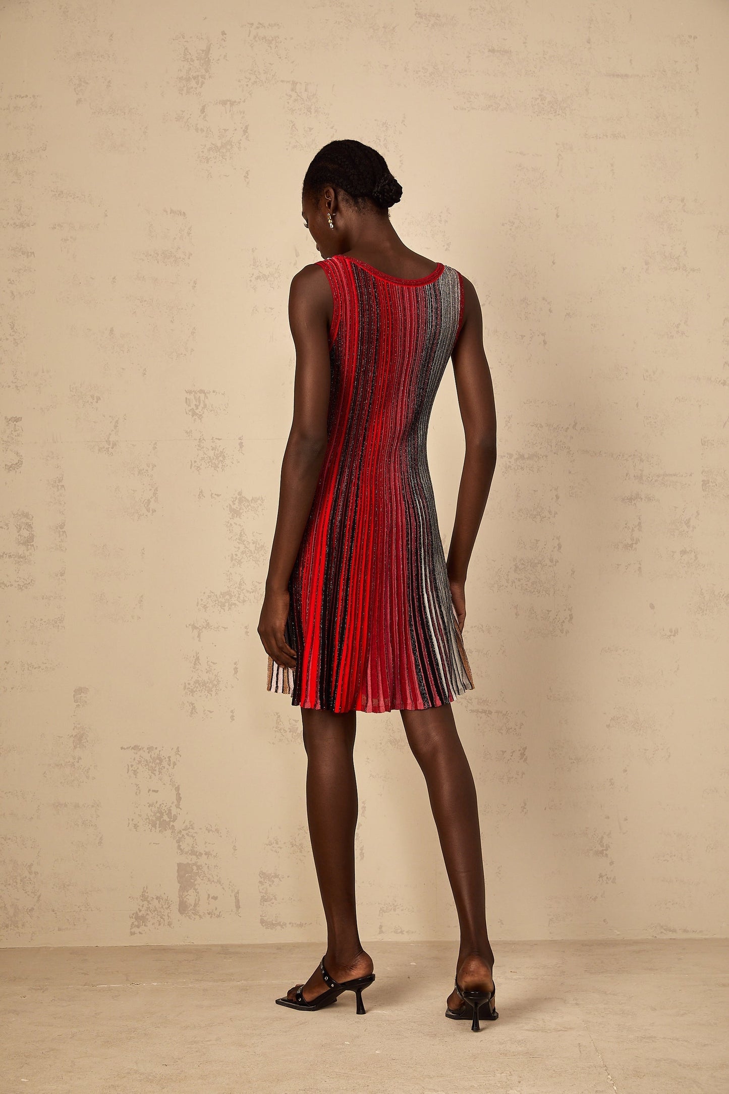 A woman wearing a red mini dress with sequin stripes standing against a plain background The dress features a knit texture and a short hemline showcasing the legs