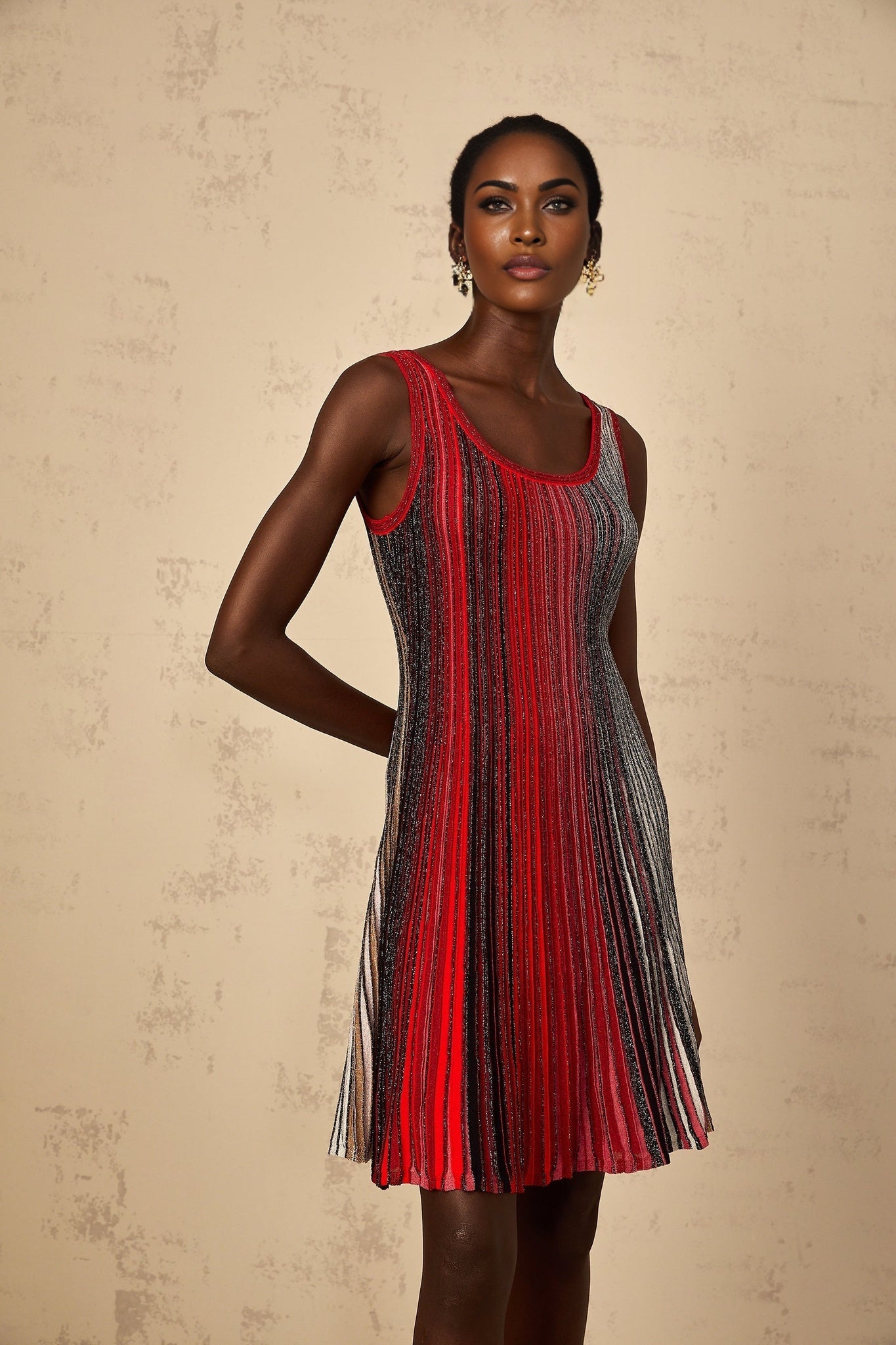 A woman wearing a red mini dress with sequin stripes standing against a plain background The dress has a knit texture and fits close to the body showcasing a short hemline