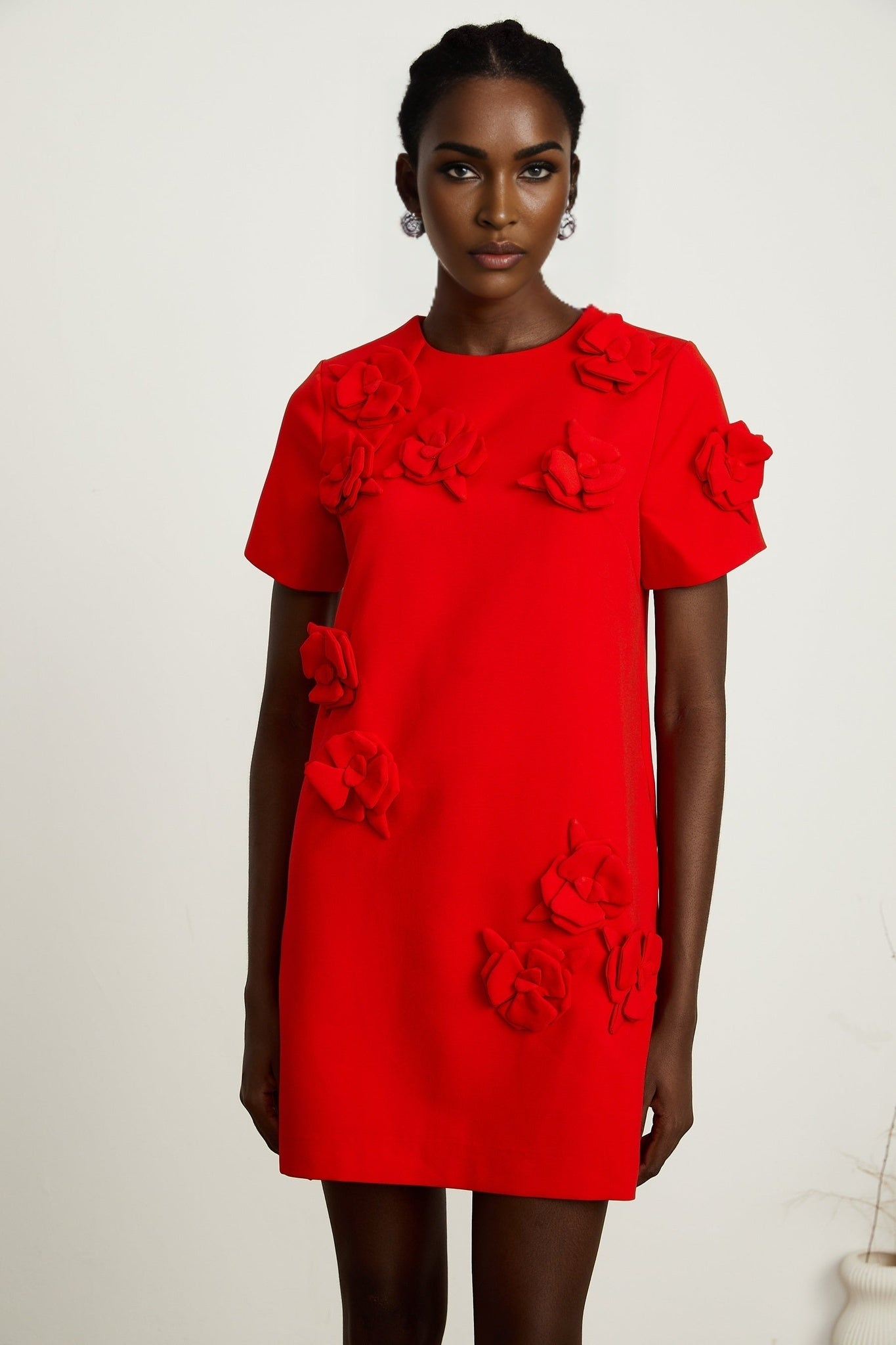 A woman wearing a red mini dress with short sleeves and floral details standing against a plain background