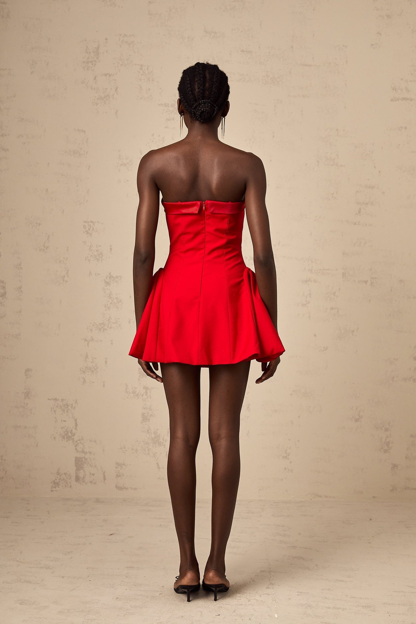 A woman wearing a red offshoulder mini dress with flared sleeves and a short skirt posing against a plain background