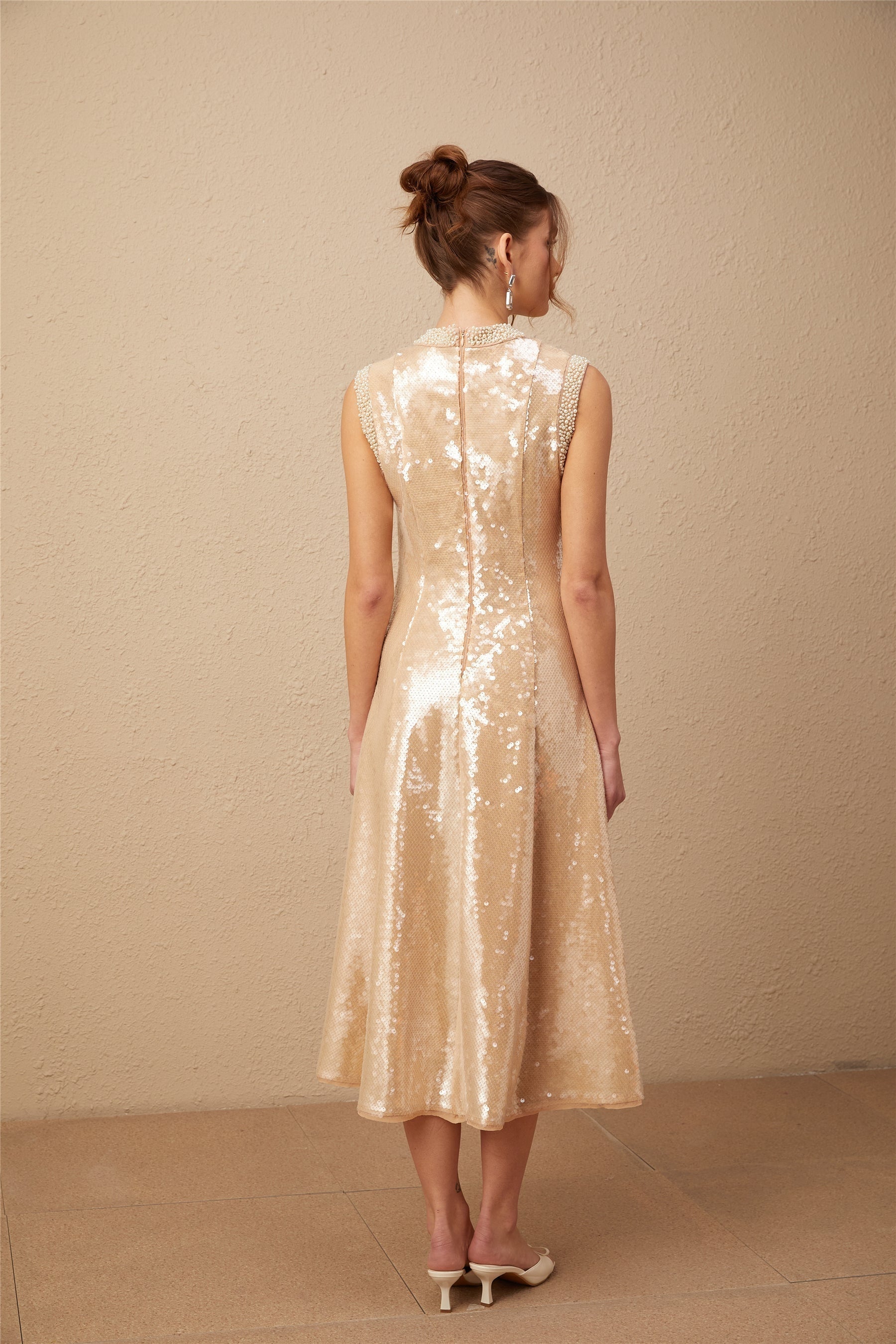 A woman wearing a shimmering midi dress adorned with faux pearls and sequins elegant evening attire with a feminine silhouette