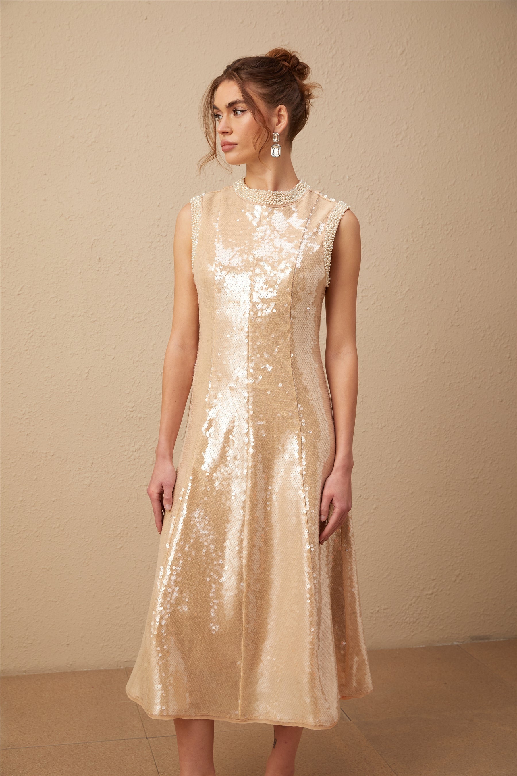 A woman wearing a shimmering midi dress adorned with faux pearls and sequins posing elegantly against a plain background