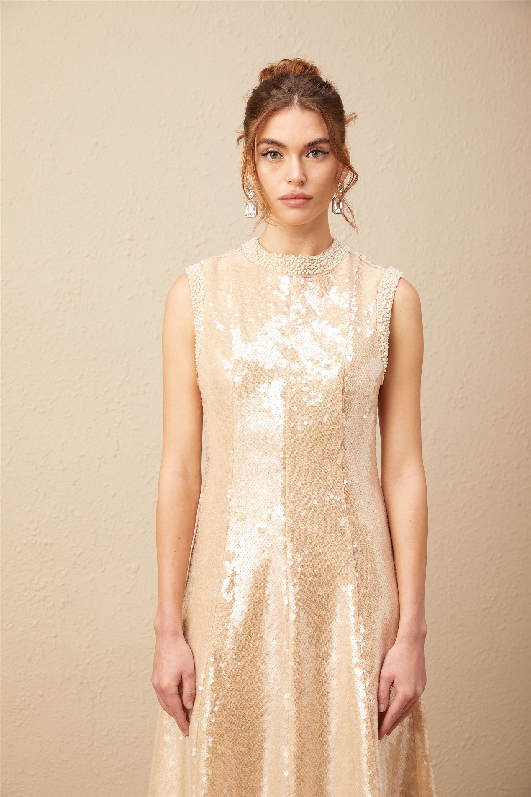 A woman wearing a shimmering midi dress adorned with faux pearls and sequins posing elegantly against a plain background