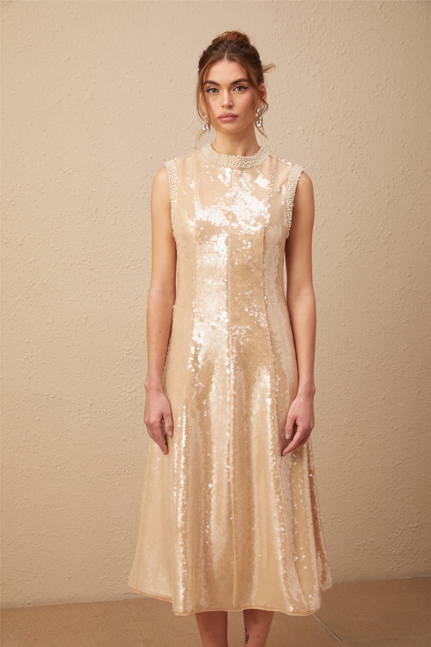 A woman wearing a shimmering midi dress adorned with faux pearls and sequins standing against a plain background