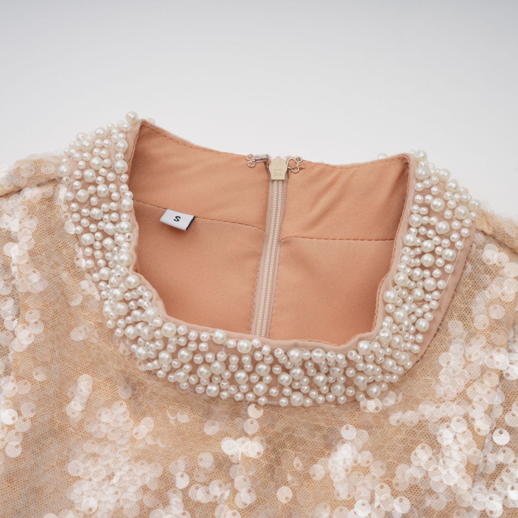 A woman wearing a shimmering midi dress adorned with faux pearls and sequins standing against a plain background