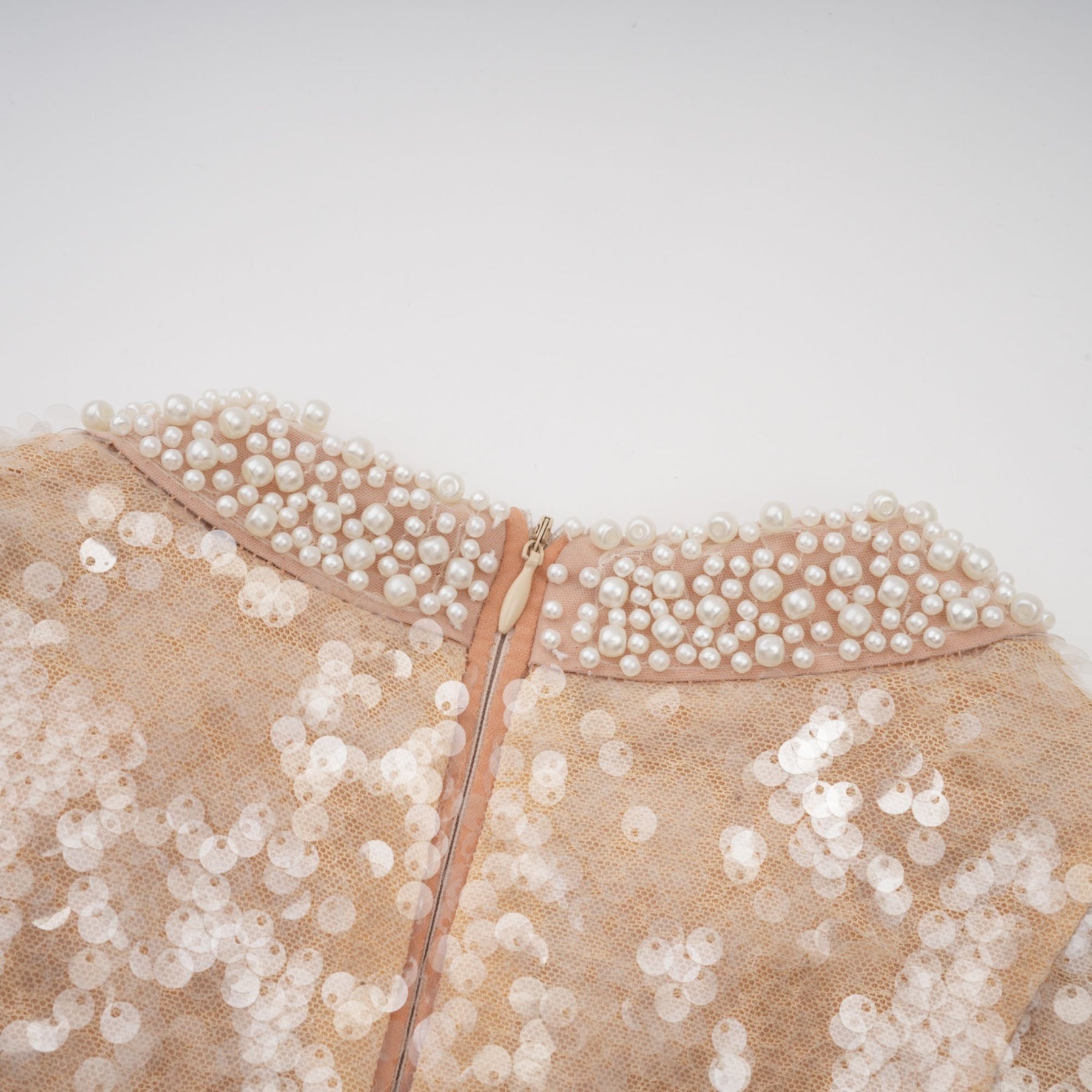 A woman wearing a shimmering midi dress adorned with faux pearls and sequins standing in an elegant pose