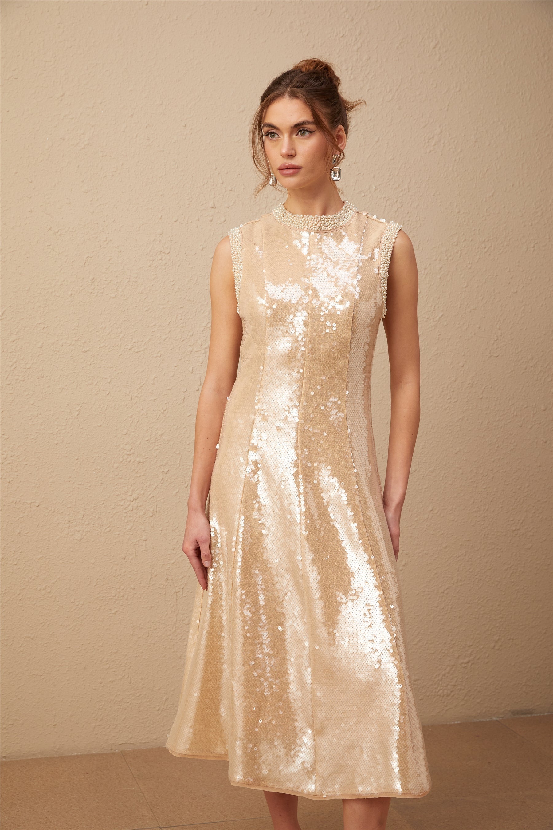 A woman wearing a shimmering midi dress adorned with faux pearls and sequins standing in an elegant pose