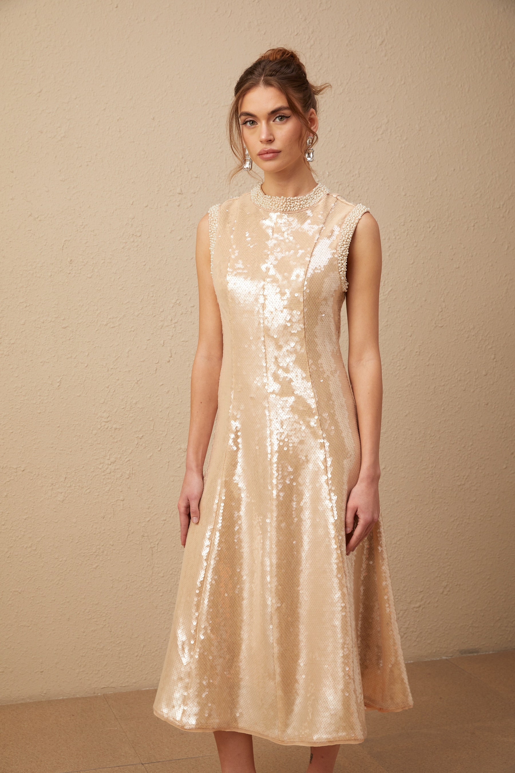 A woman wearing a shimmering midi dress adorned with sequins and faux pearls standing in an elegant pose