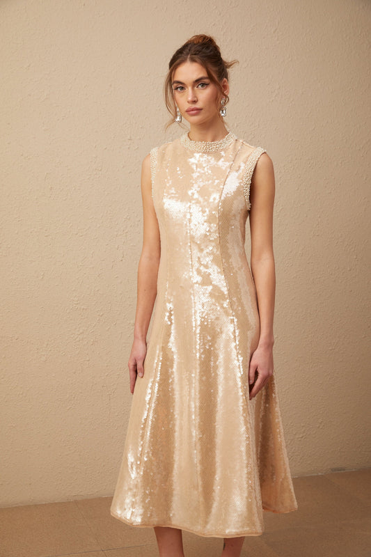 A woman wearing a shimmering midi dress adorned with sequins and faux pearls standing in an elegant pose
