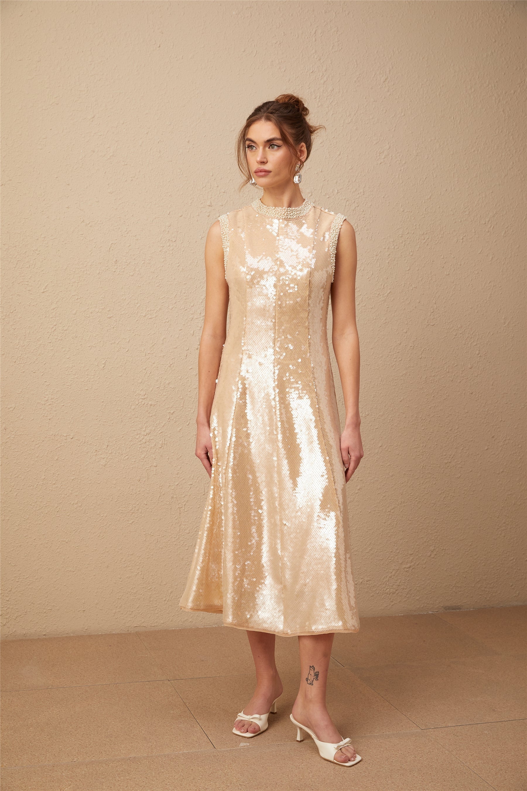 A woman wearing a shimmering midi dress with faux pearl and sequin embellishments standing in an elegant pose