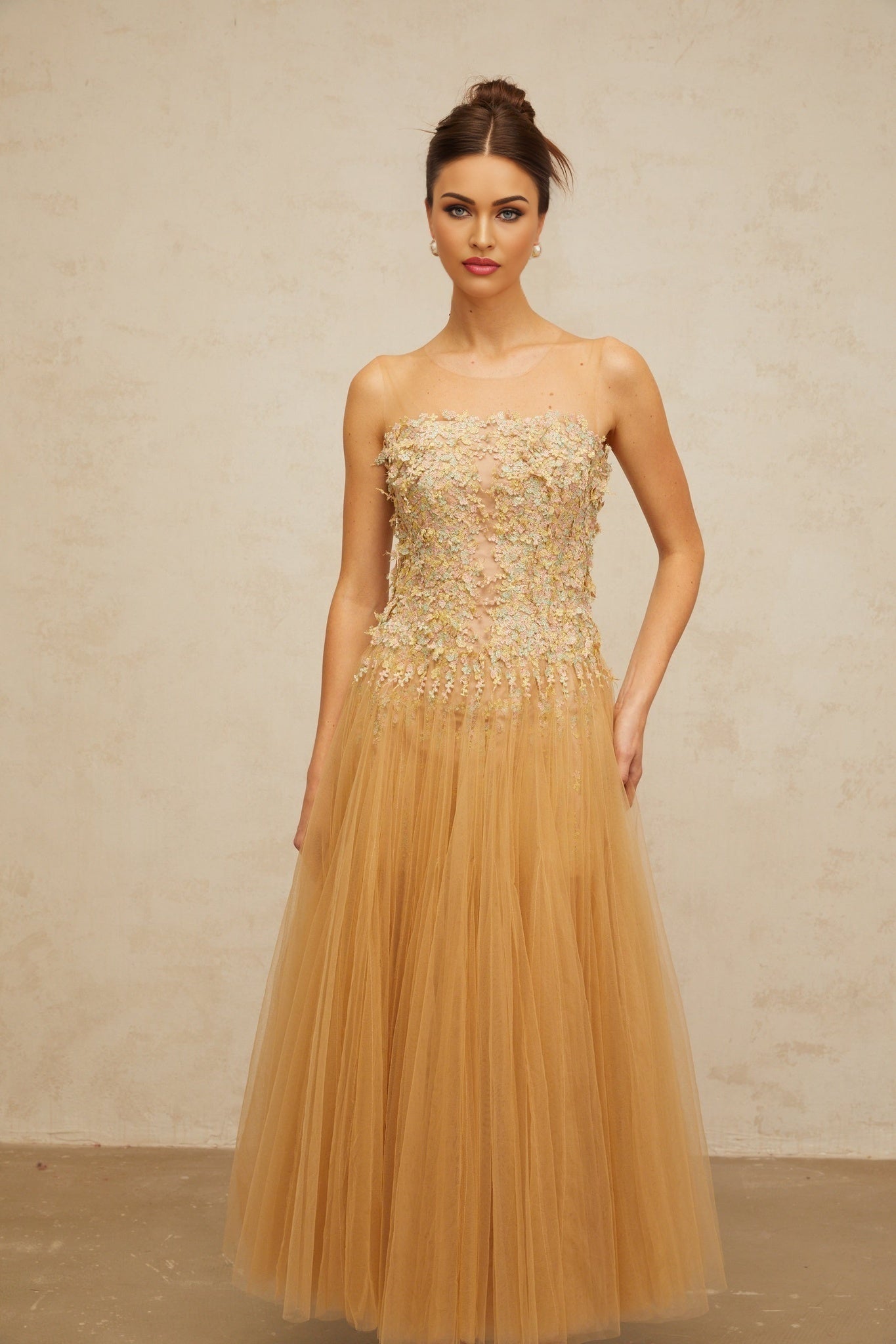 A woman wearing a shimmering neutralcolored midi dress with pleated tulle and sequin embellishments standing in a relaxed pose