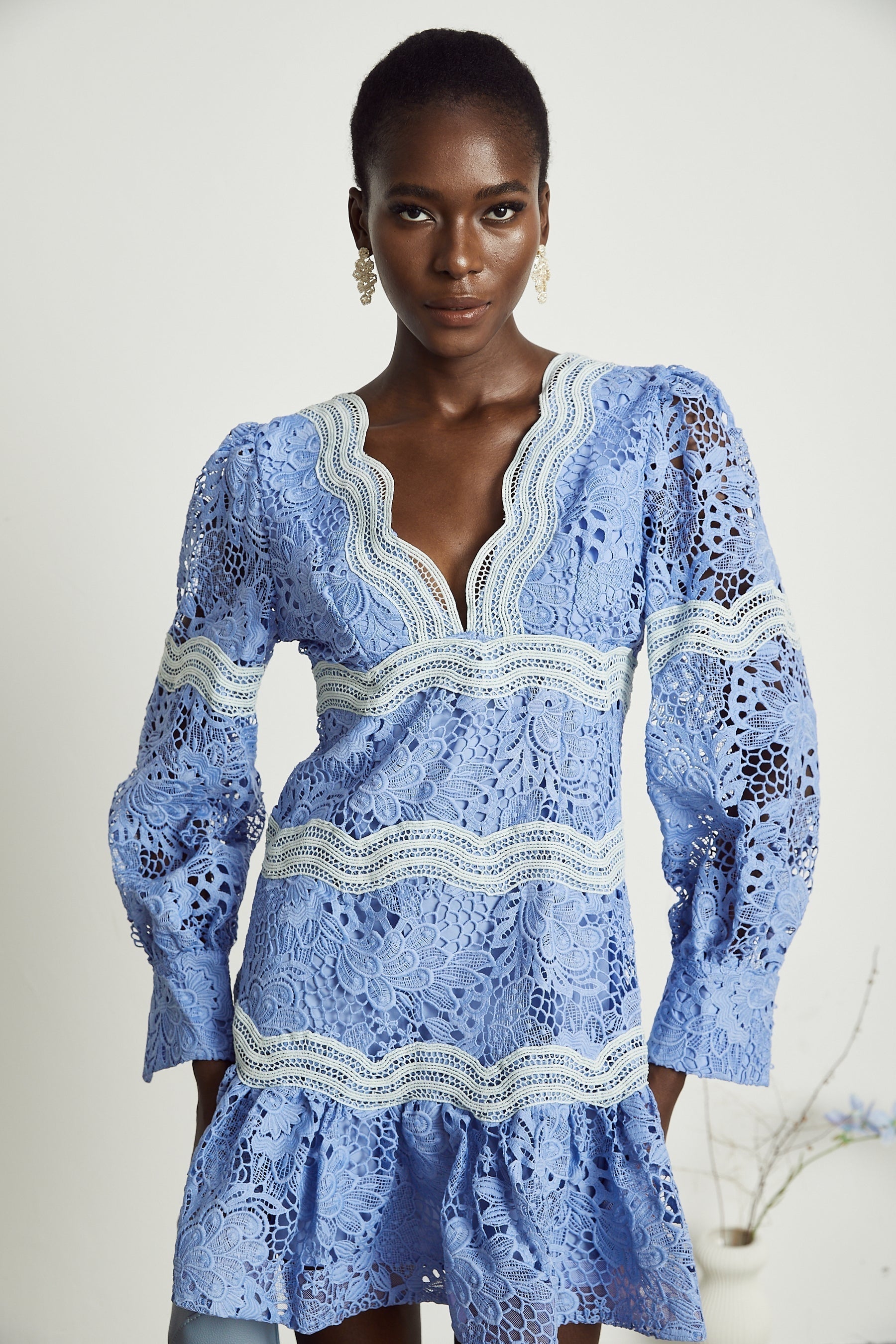 A woman wearing a short floral embroidered mini dress with a V neckline the dress has a vibrant pattern and fitted silhouette