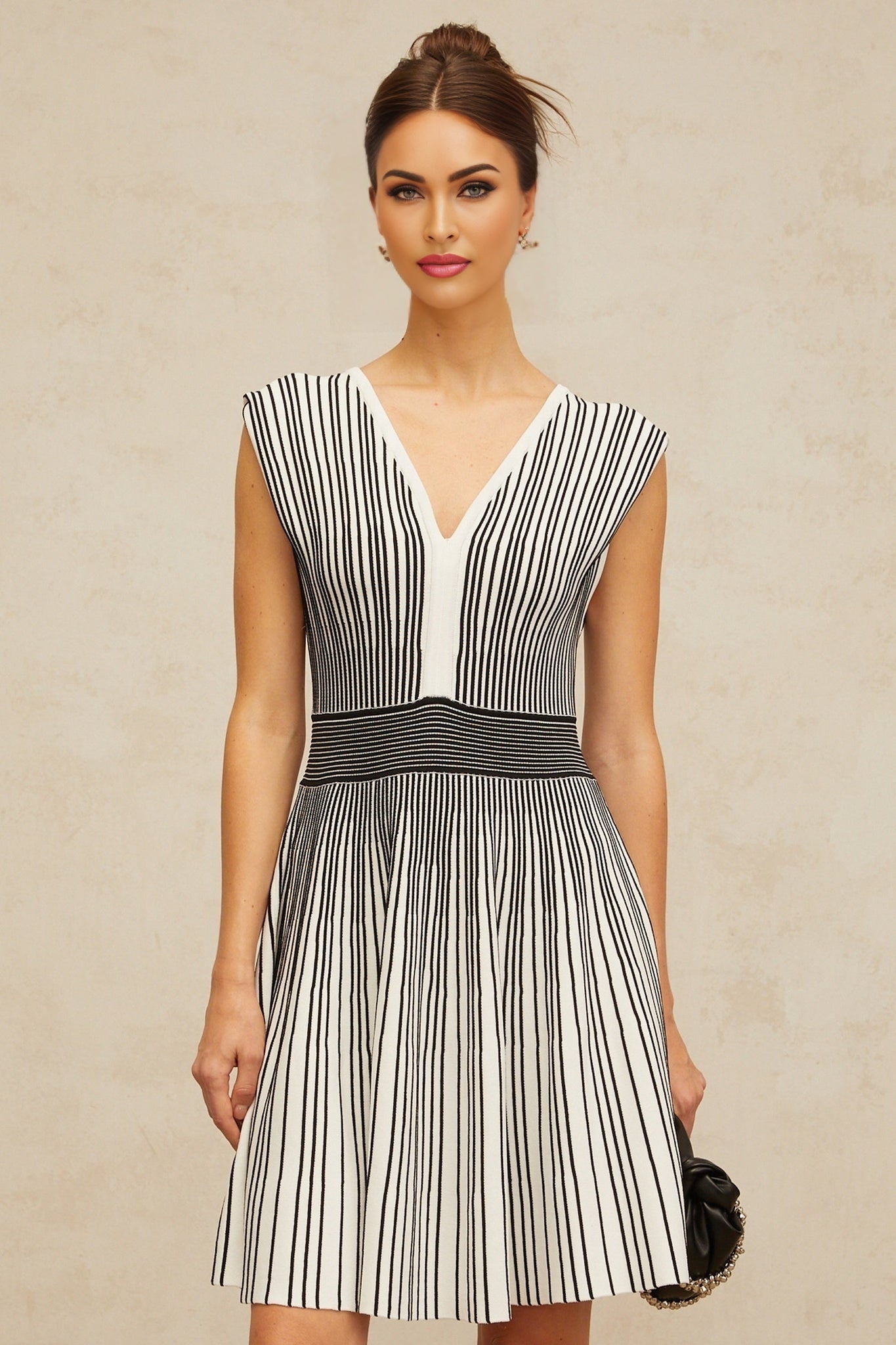 A woman wearing a short knitted dress with vertical stripes in contrasting colors standing against a plain background