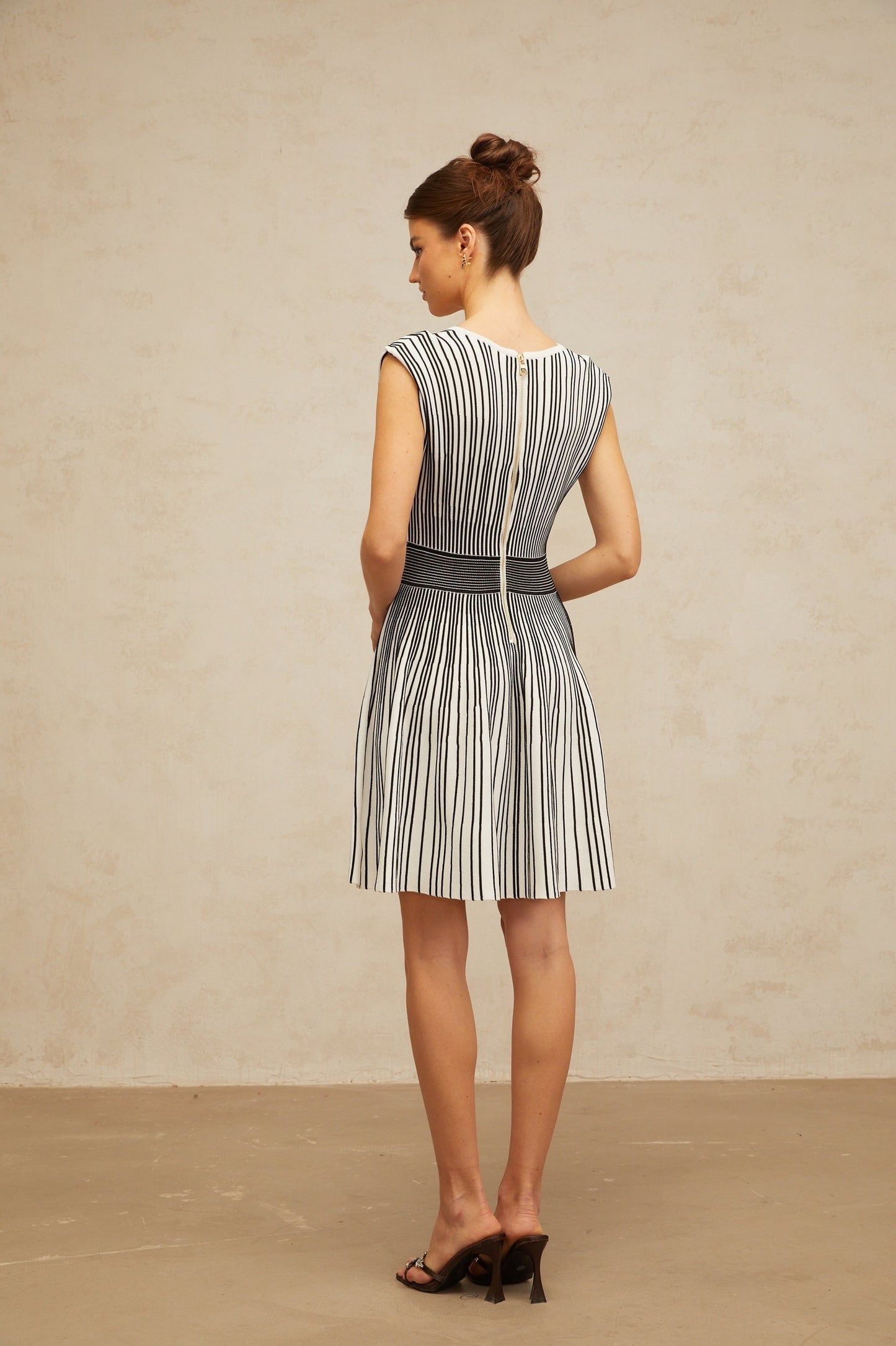 A woman wearing a short knitted dress with vertical stripes in contrasting colors standing against a plain background