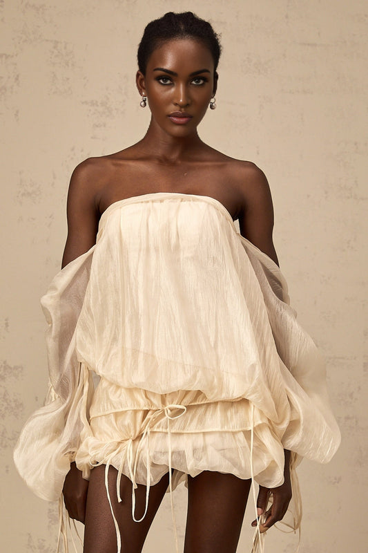 A woman wearing a short offshoulder dress with ruched detailing and layered fabric The dress has selftie straps and falls above the knee