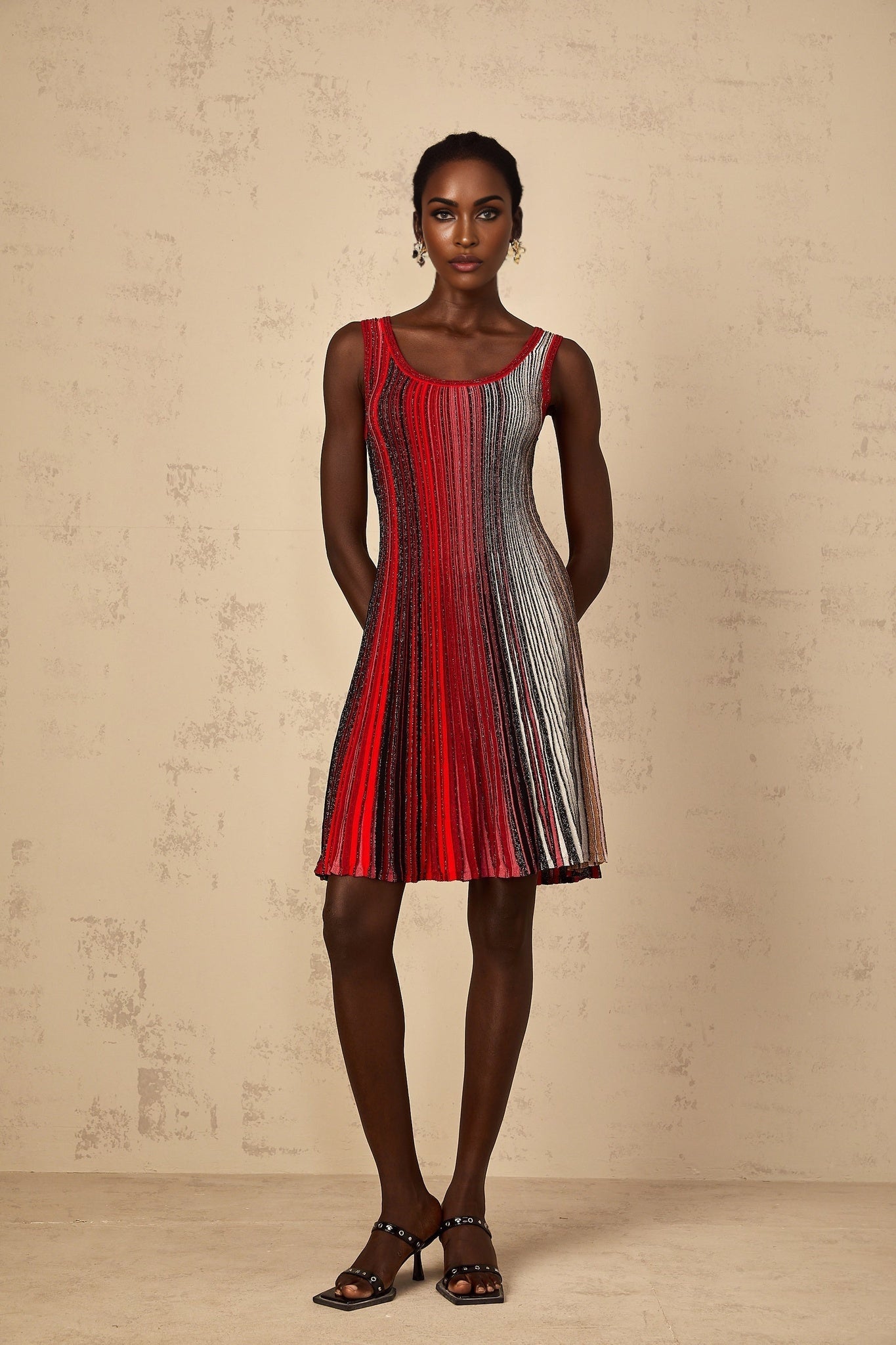 A woman wearing a short red knit dress with sequin stripes standing against a plain background