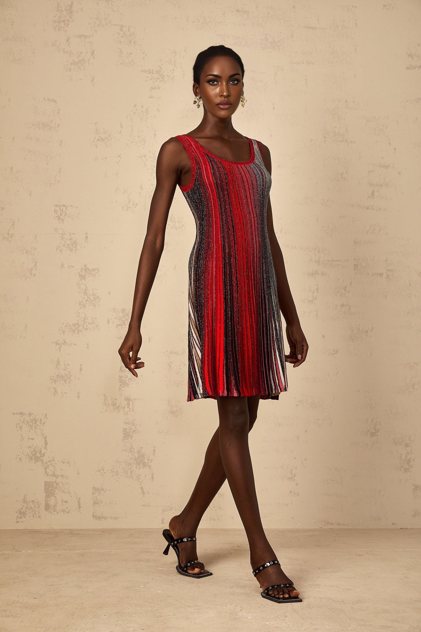A woman wearing a short red knit dress with vertical sequin stripes standing against a plain background