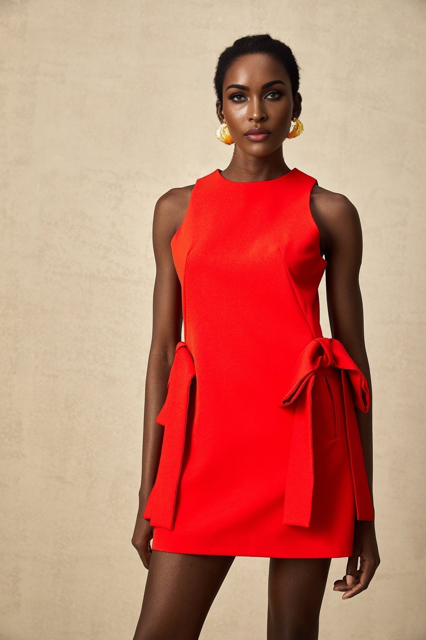A woman wearing a short red sleeveless dress with a bow detail