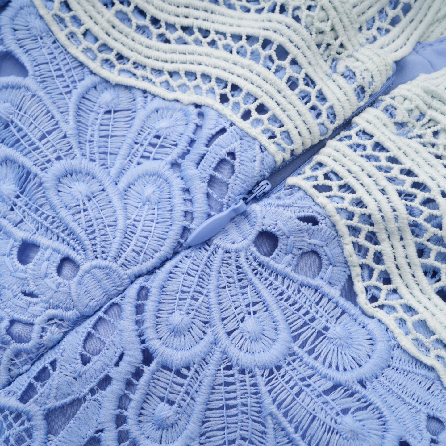 A woman wearing a short white mini dress with a Vneck and colorful floral embroidery detail standing against a plain background