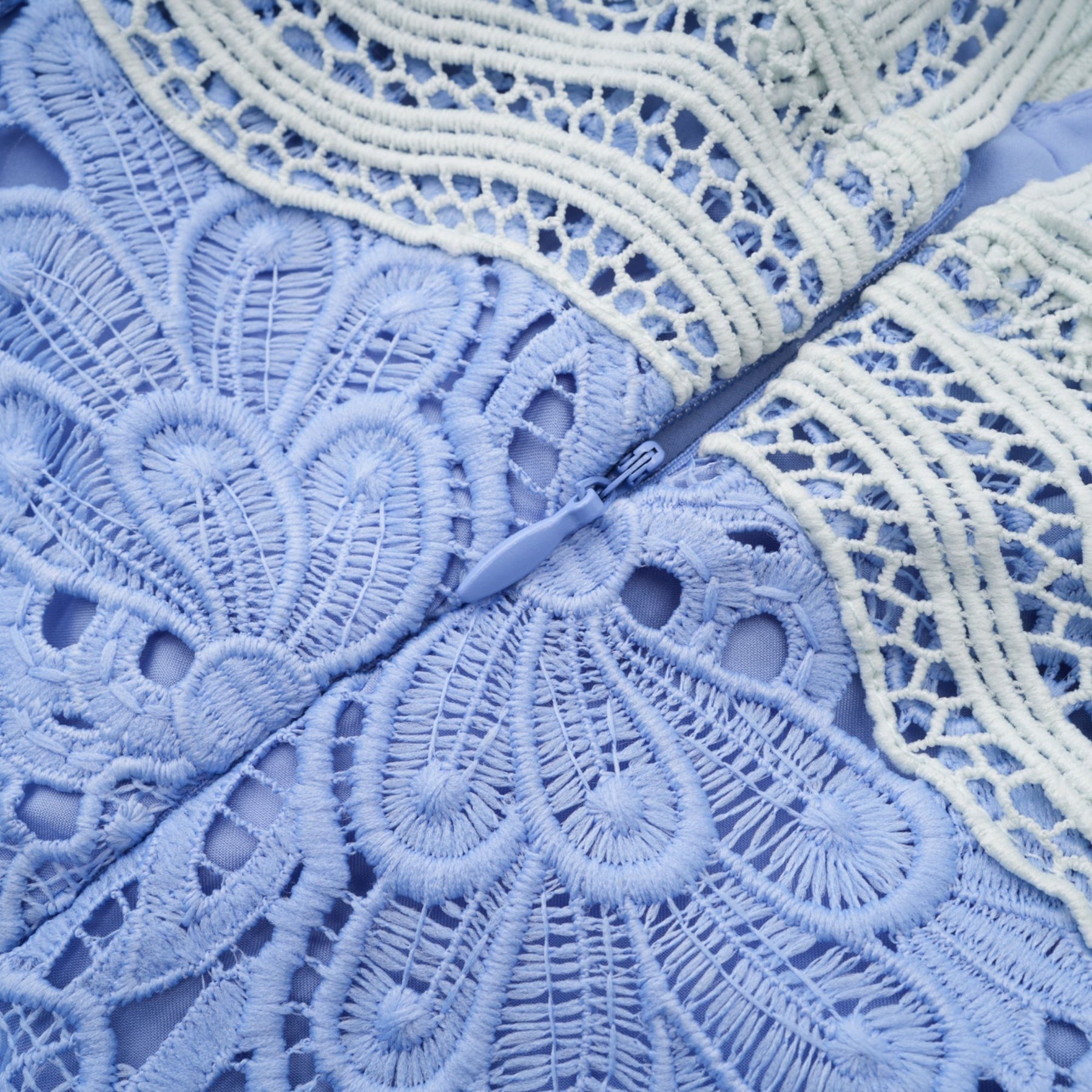 A woman wearing a short white mini dress with a Vneck and colorful floral embroidery detail standing against a plain background