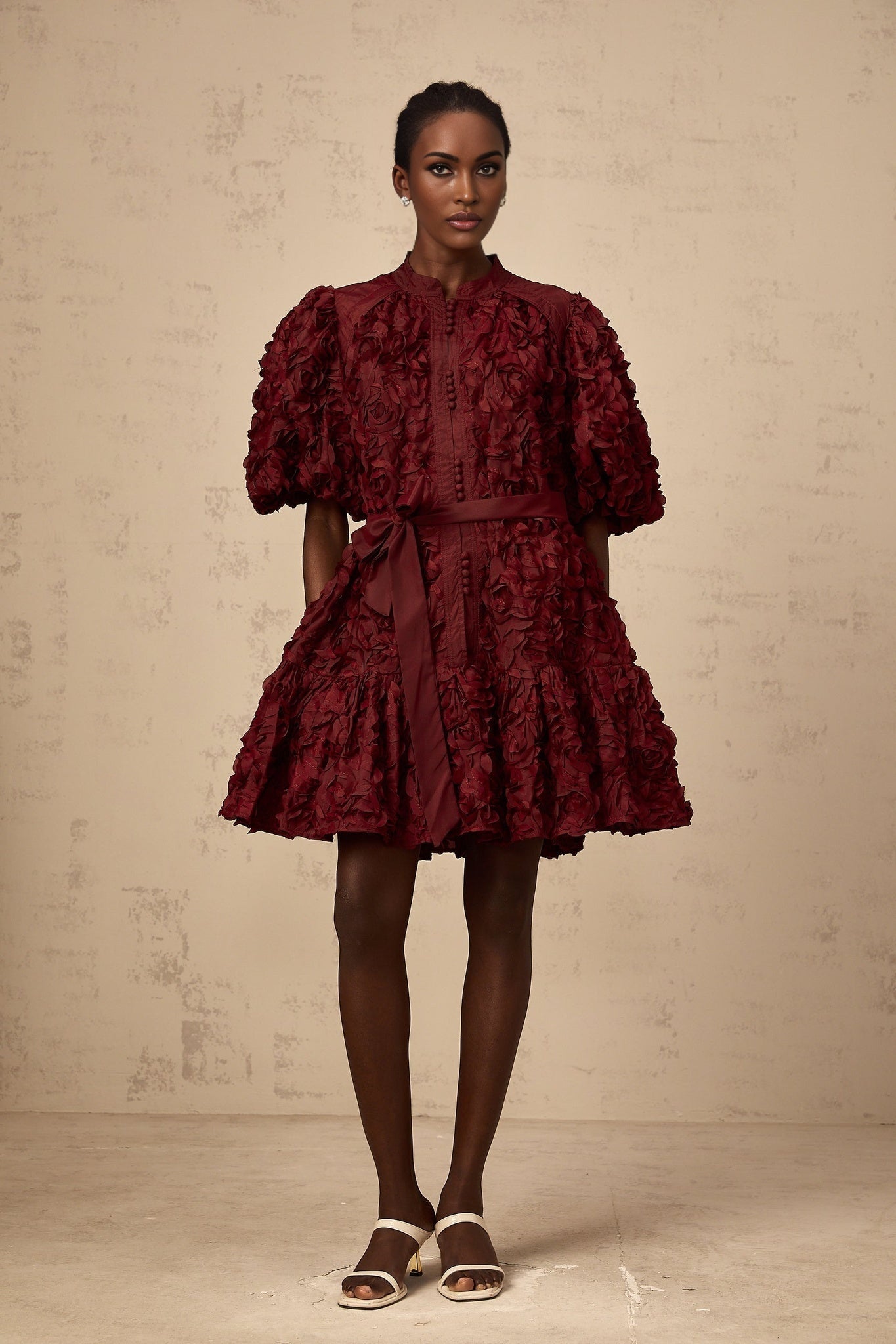 A woman wearing a short winered dress with three dimensional petal like puffs covering the fabric creating texture and volume