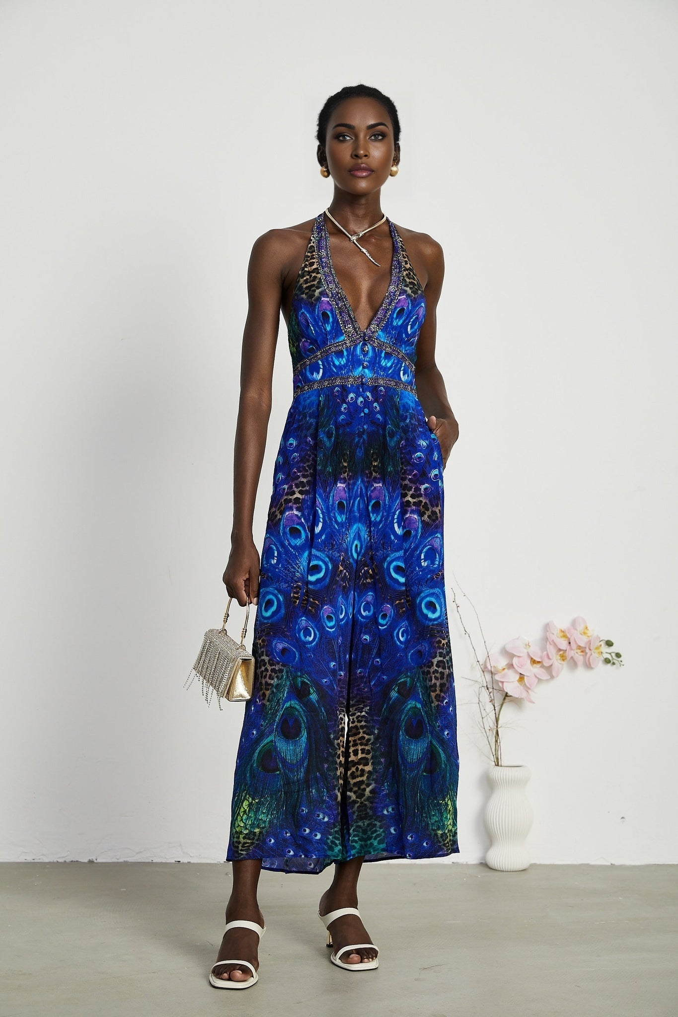 A woman wearing a sleek silk jumpsuit with a halter neckline in a stylish silhouette standing in a relaxed pose against a plain background