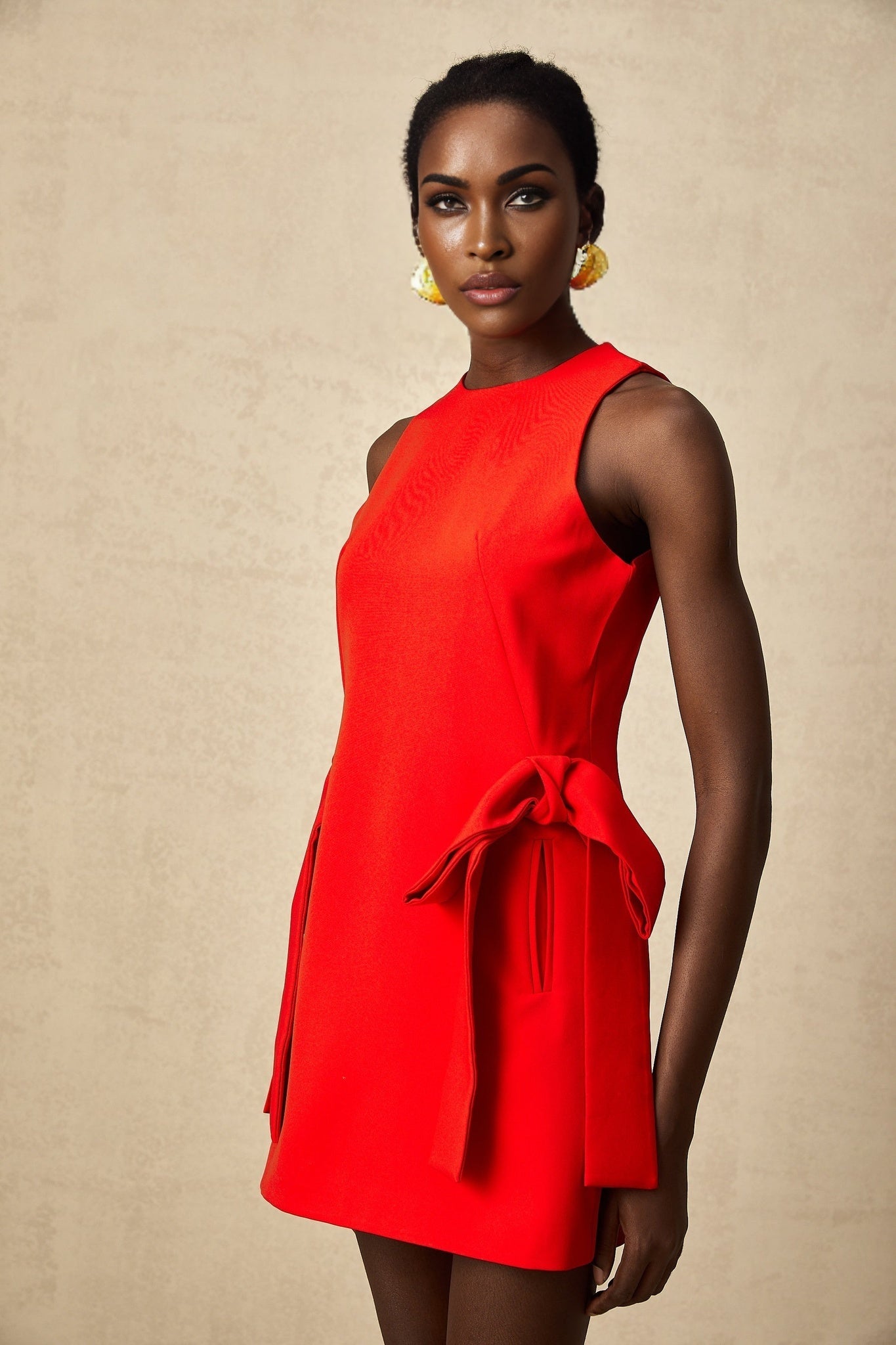 A woman wearing a sleeveless red mini dress with a bow detail