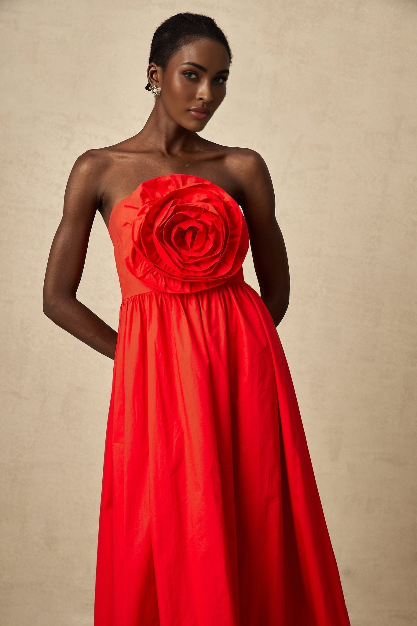 A woman wearing a vibrant red maxi dress with ruffled three dimensional petal details cascading down the length of the gown