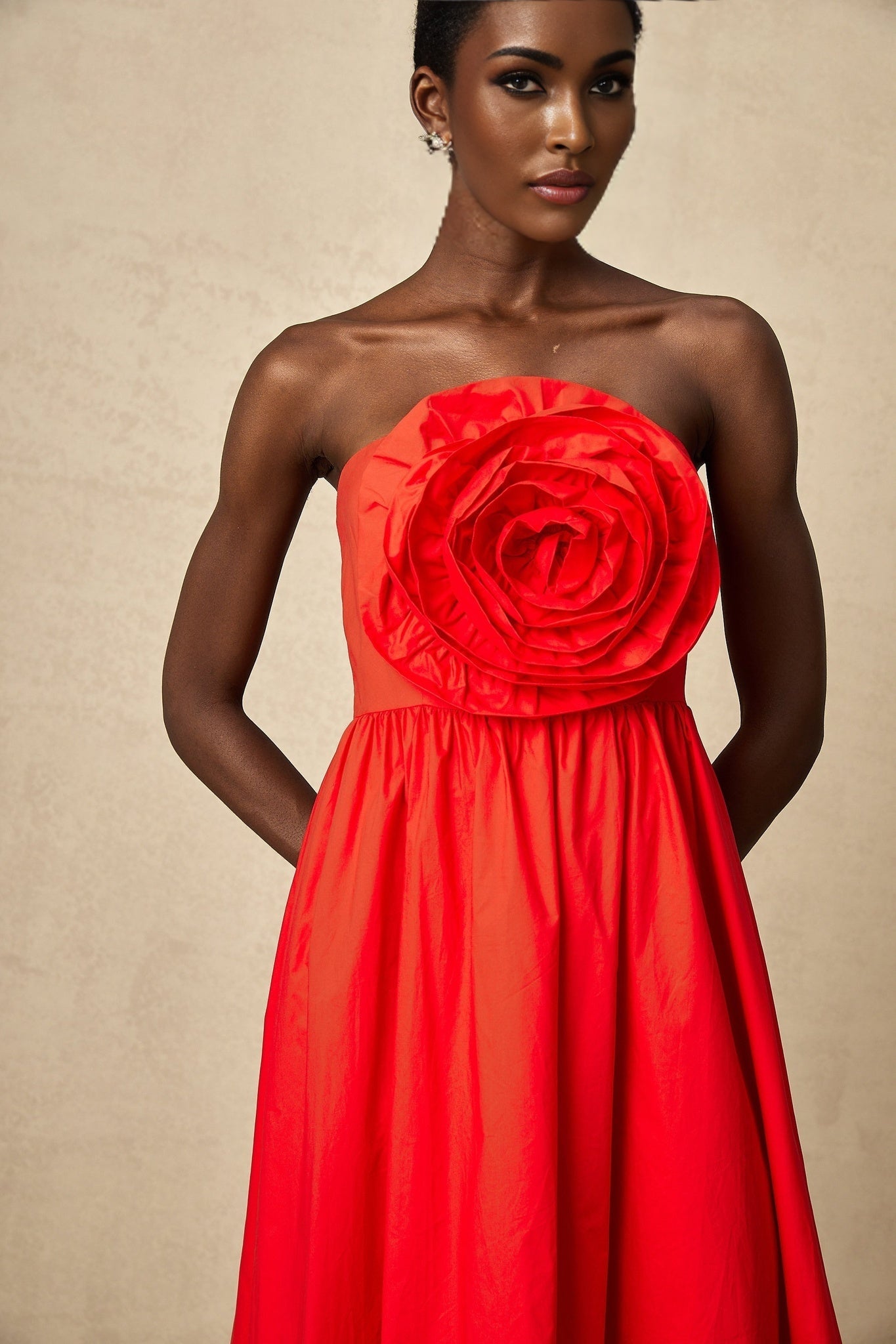 A woman wearing a vibrant red maxi dress with three dimensional petallike ruffles cascading down the length of the gown