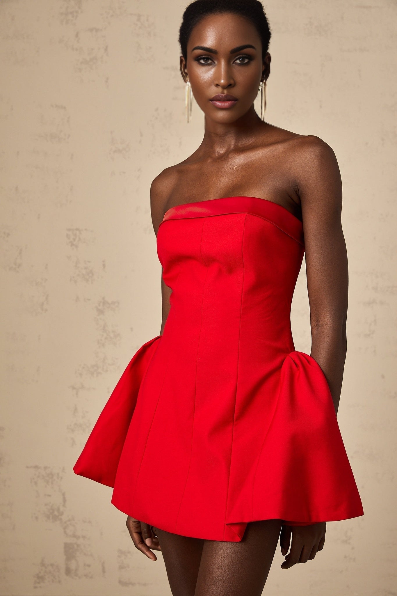 A woman wearing a vibrant red off shoulder mini dress with a flared skirt standing against a plain background