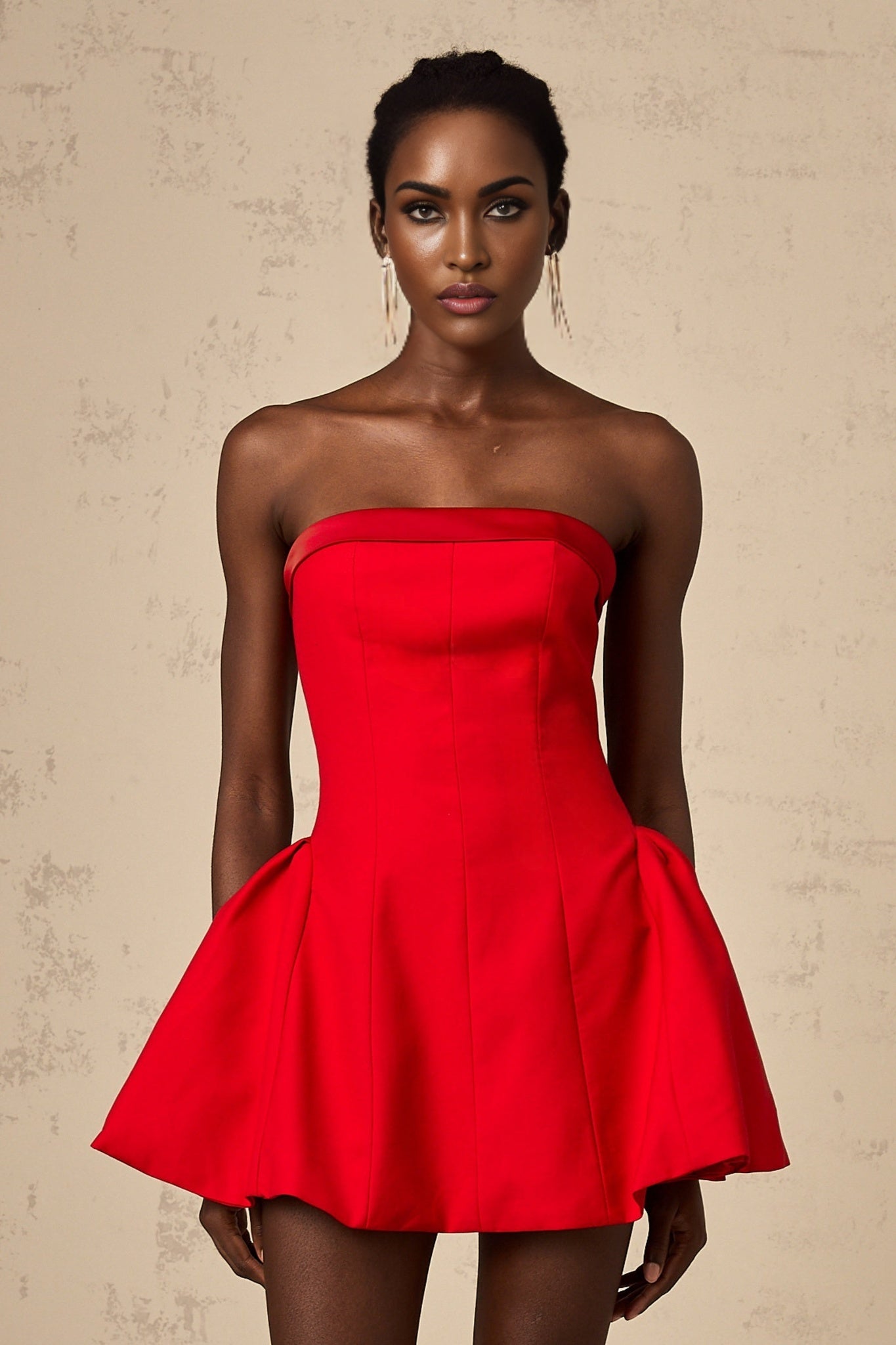 A woman wearing a vibrant red offshoulder mini dress with a flared skirt standing against a plain background