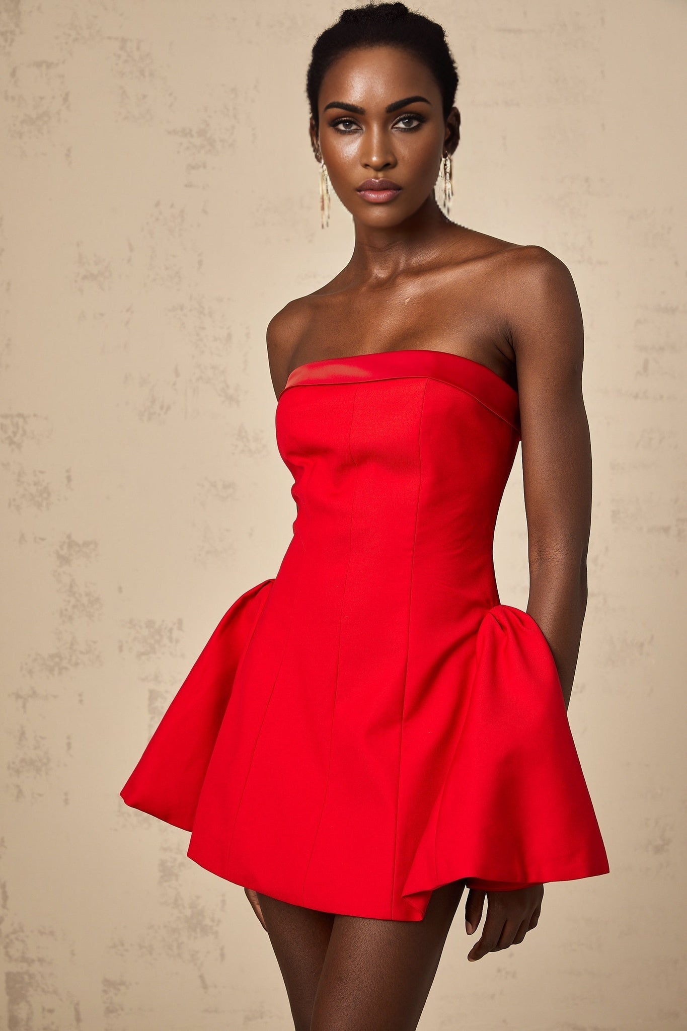 A woman wearing a vibrant red offshoulder mini dress with a flared skirt standing against a plain background