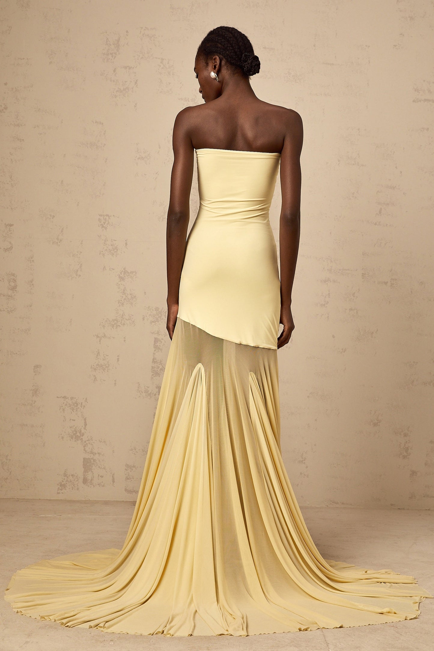 A woman wearing a vibrant yellow offshoulder maxi dress with sheer tulle details standing against a plain background