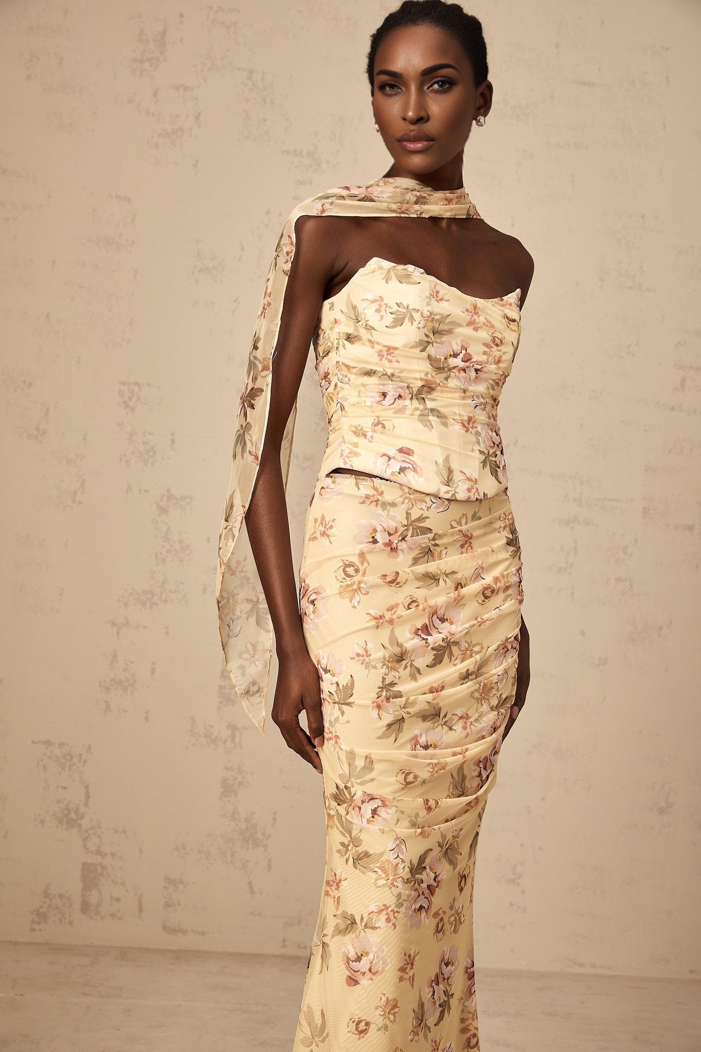 A woman wearing a vibrant yellow two piece outfit with a floral print design consisting of a fitted top and matching skirt