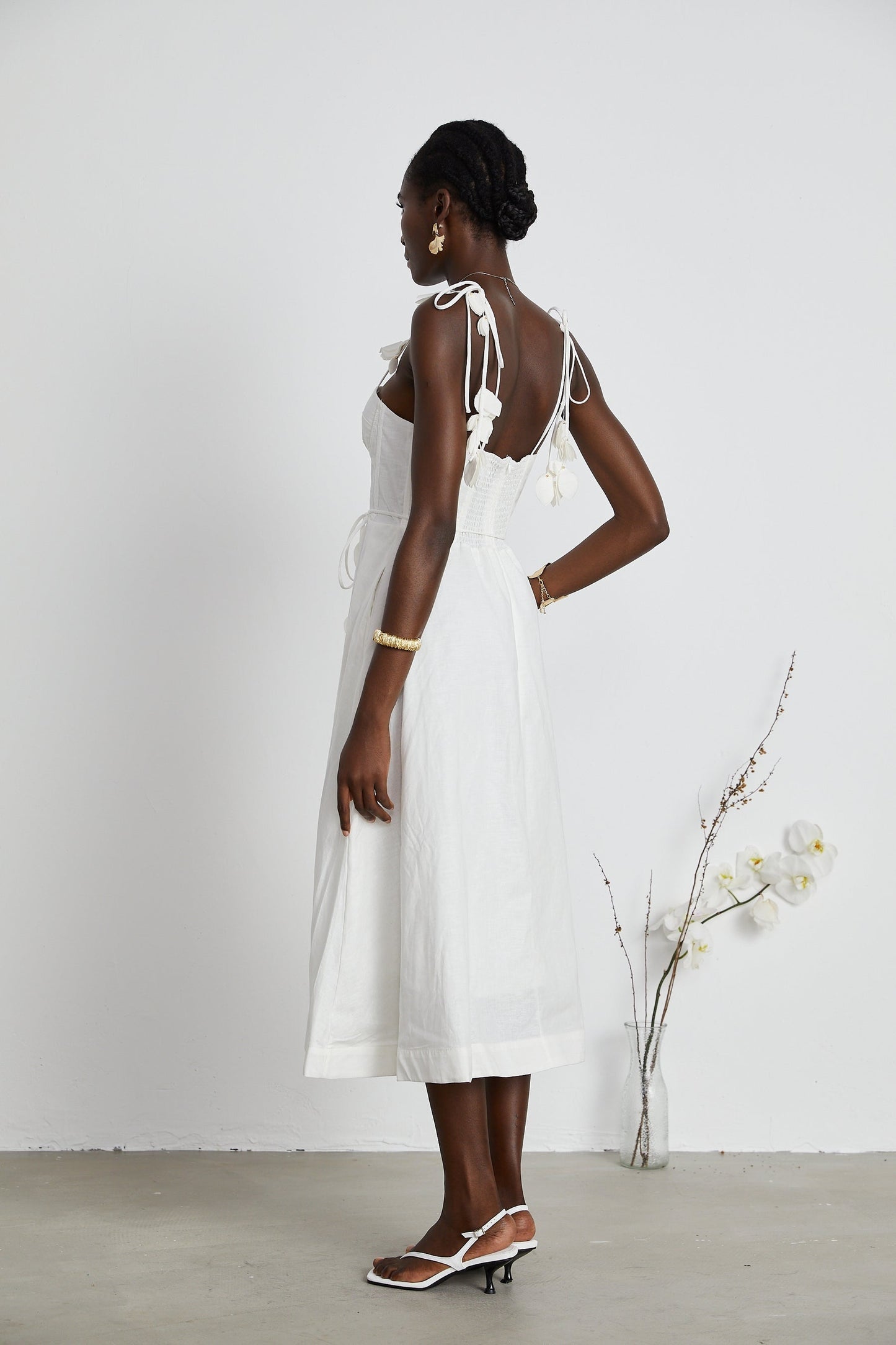 A woman wearing a white corset midi dress with a fitted bodice and flared skirt standing against a plain background
