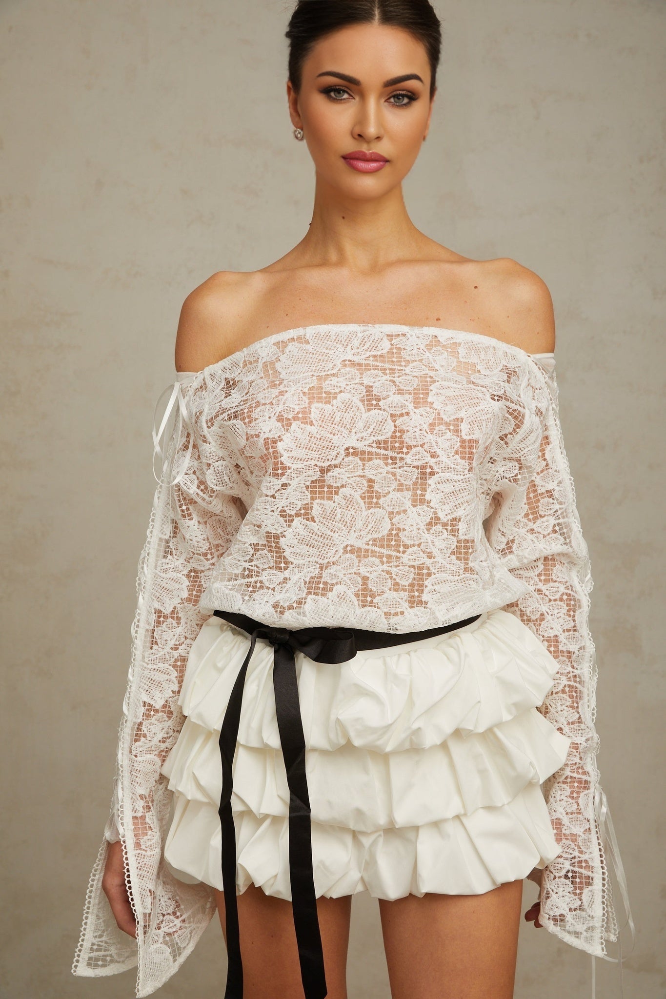 A woman wearing a white floral lace matching set consisting of a sleeveless top and a short skirt standing against a plain background