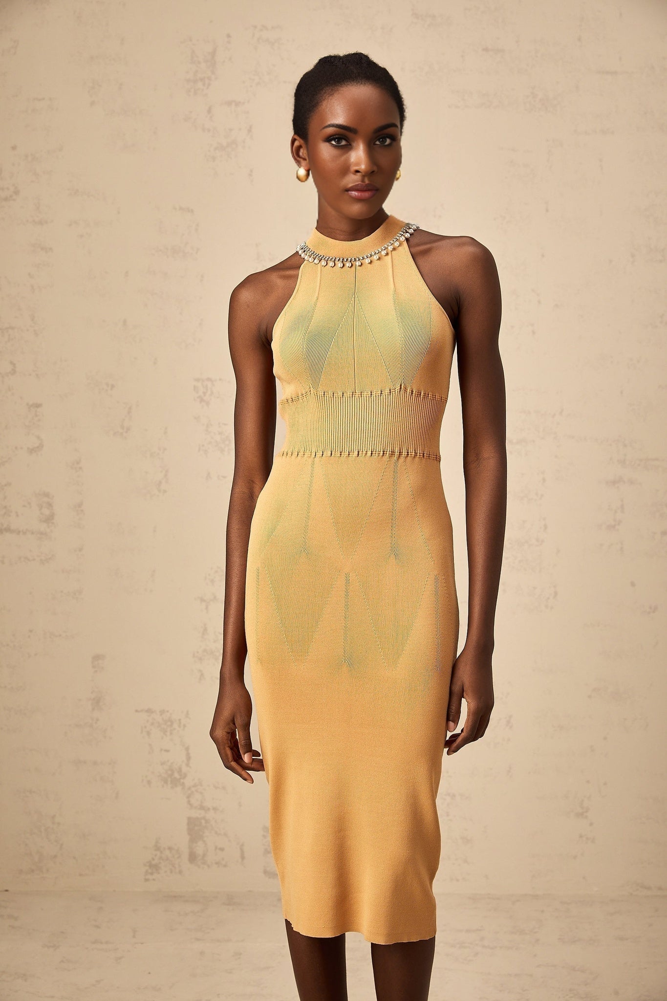 A woman wearing a white knit midi dress with faux pearl embellishments scattered across the fabric