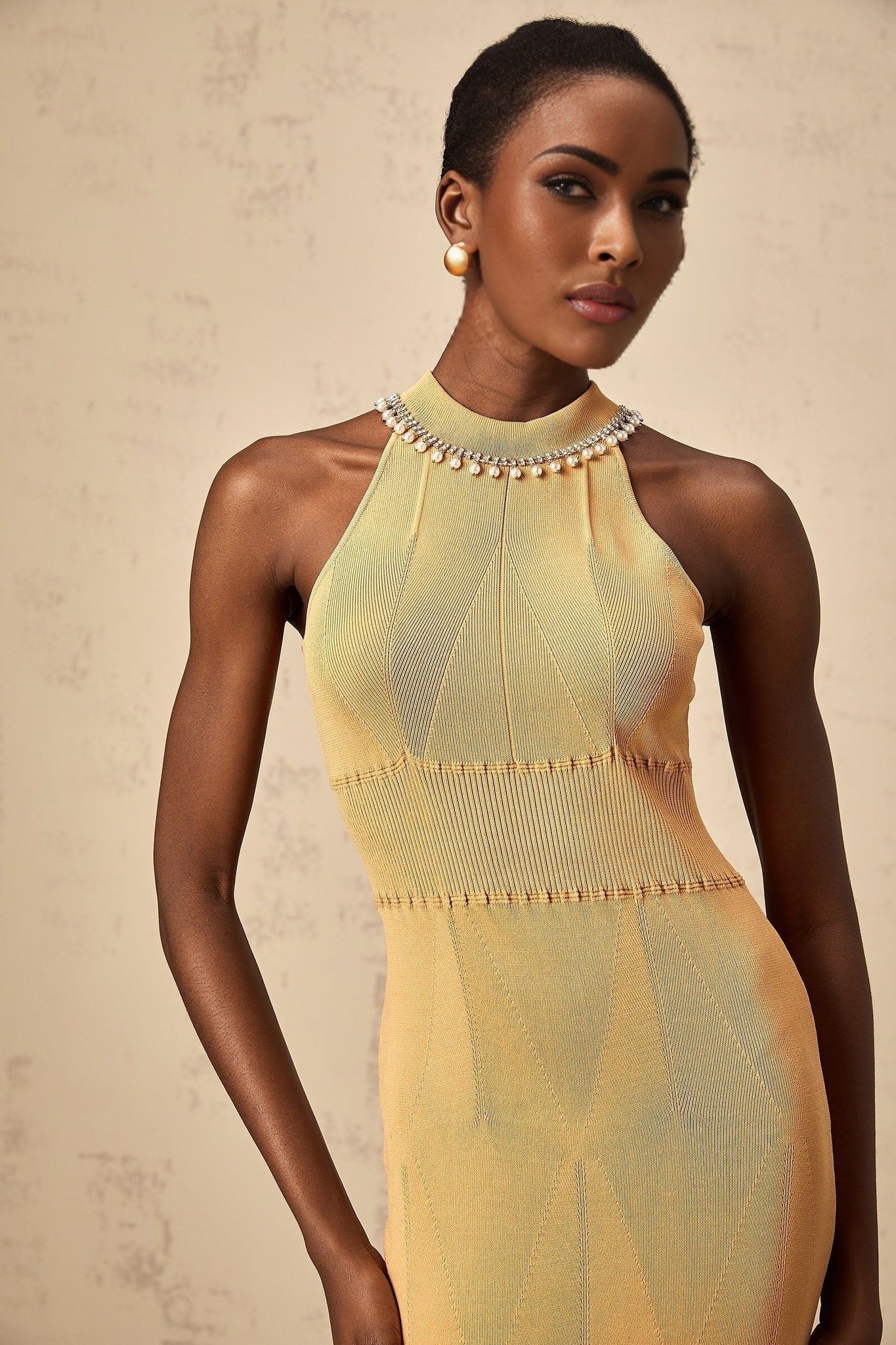 A woman wearing a white knit midi dress with faux pearl embellishments throughout the bodice and skirt