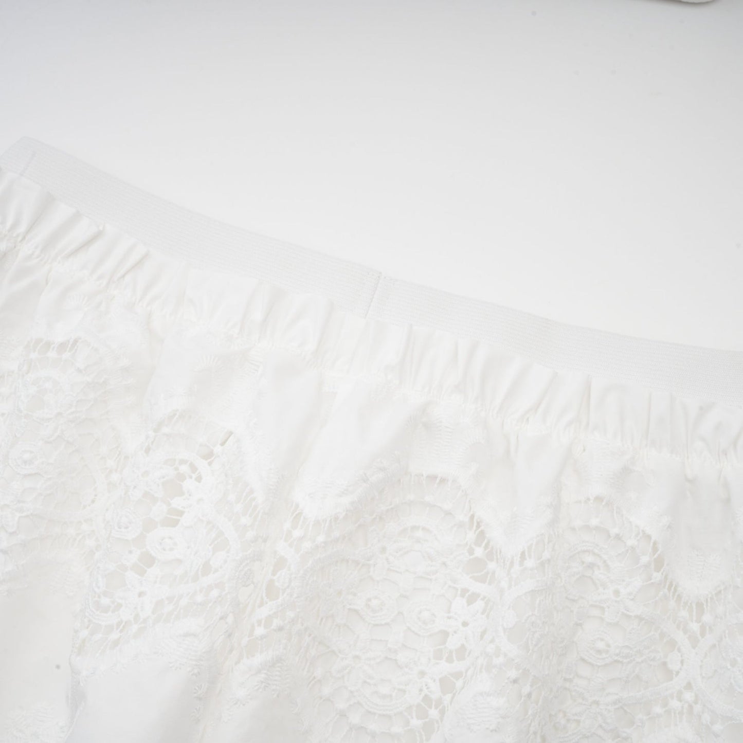 A woman wearing a white lace trimmed cropped top and matching trousers The top features cutout details and the set has a delicate feminine design