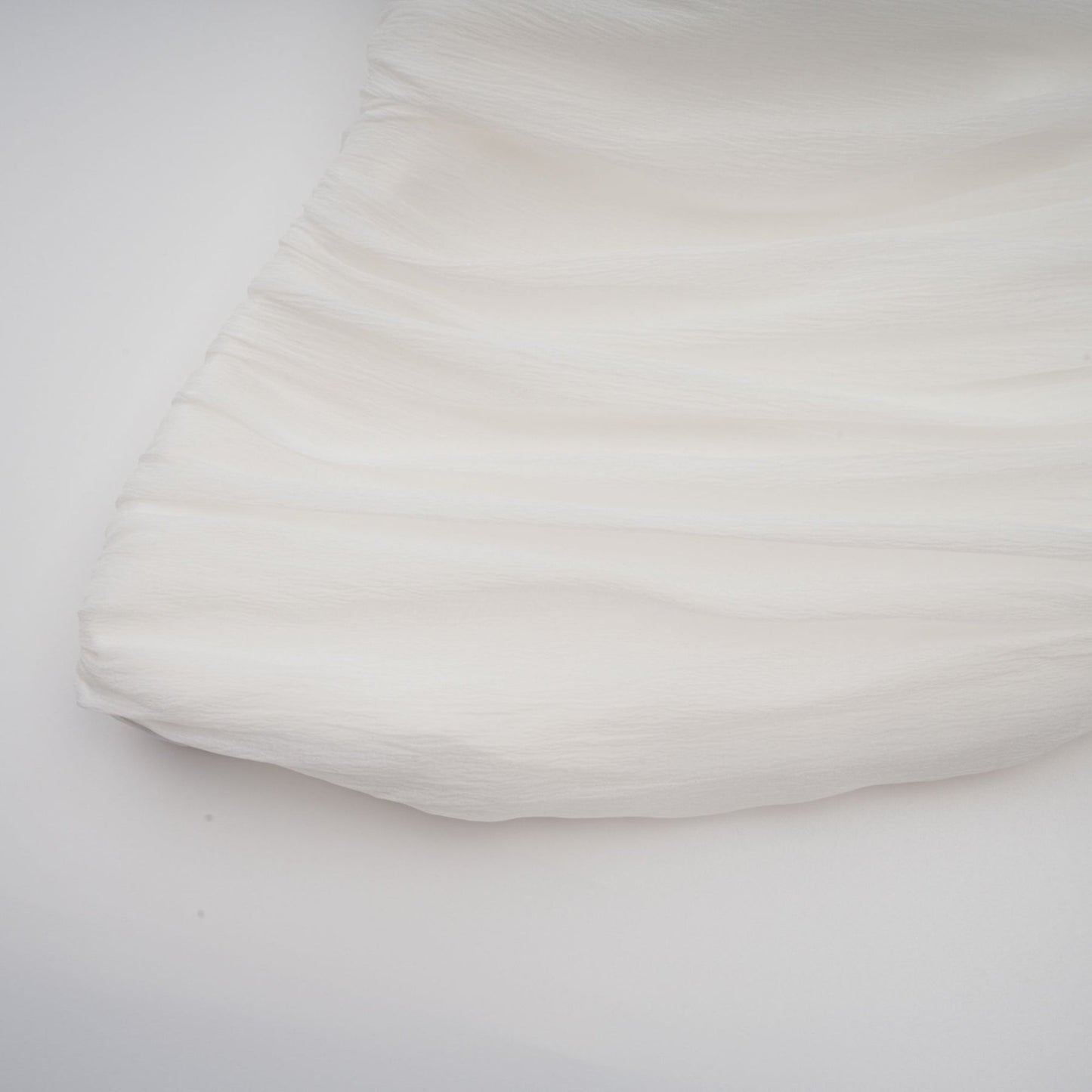 A woman wearing a white matching set consisting of a creased top and trousers standing against a plain background