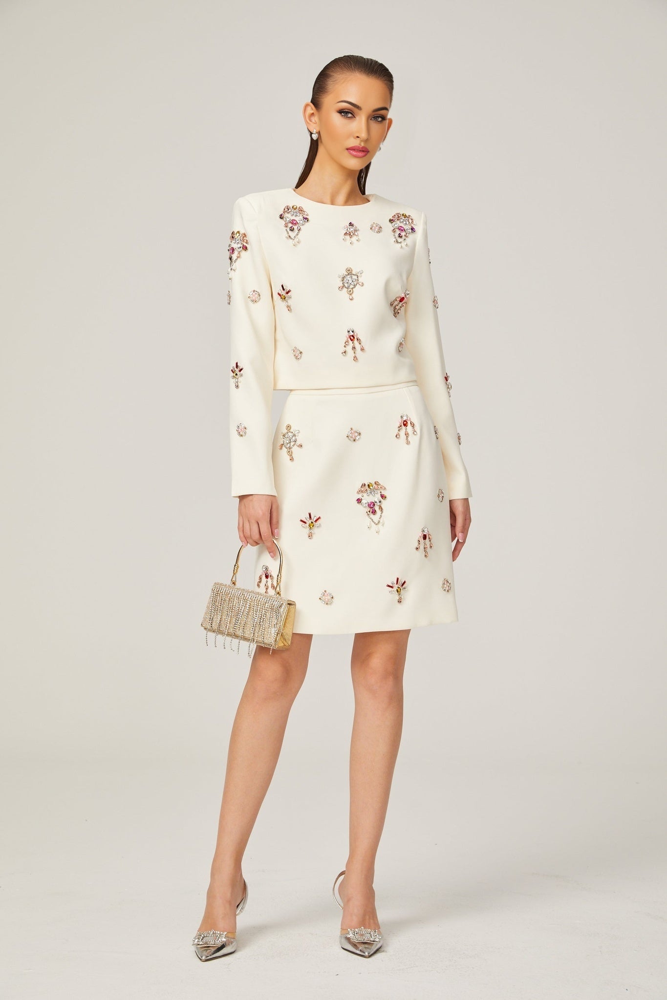 A woman wearing a white matching set consisting of a crystalembellished top and skirt named Jeanne The outfit features sparkling details and a coordinated design