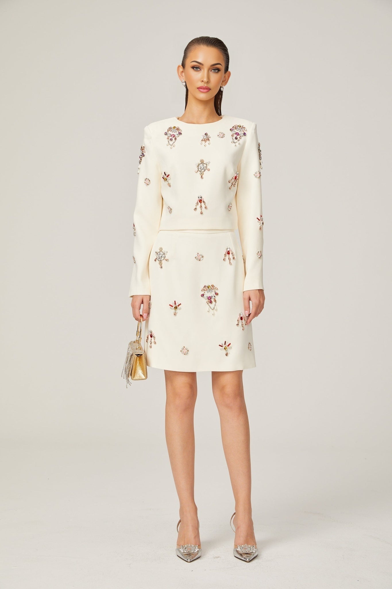 A woman wearing a white matching set consisting of a sleeveless top and skirt adorned with crystal embellishments