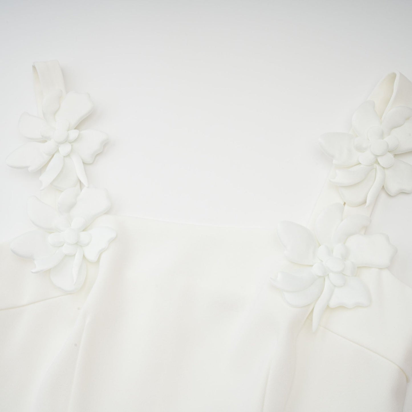 A woman wearing a white midi dress with a square neckline adorned with faux flowers standing against a plain background