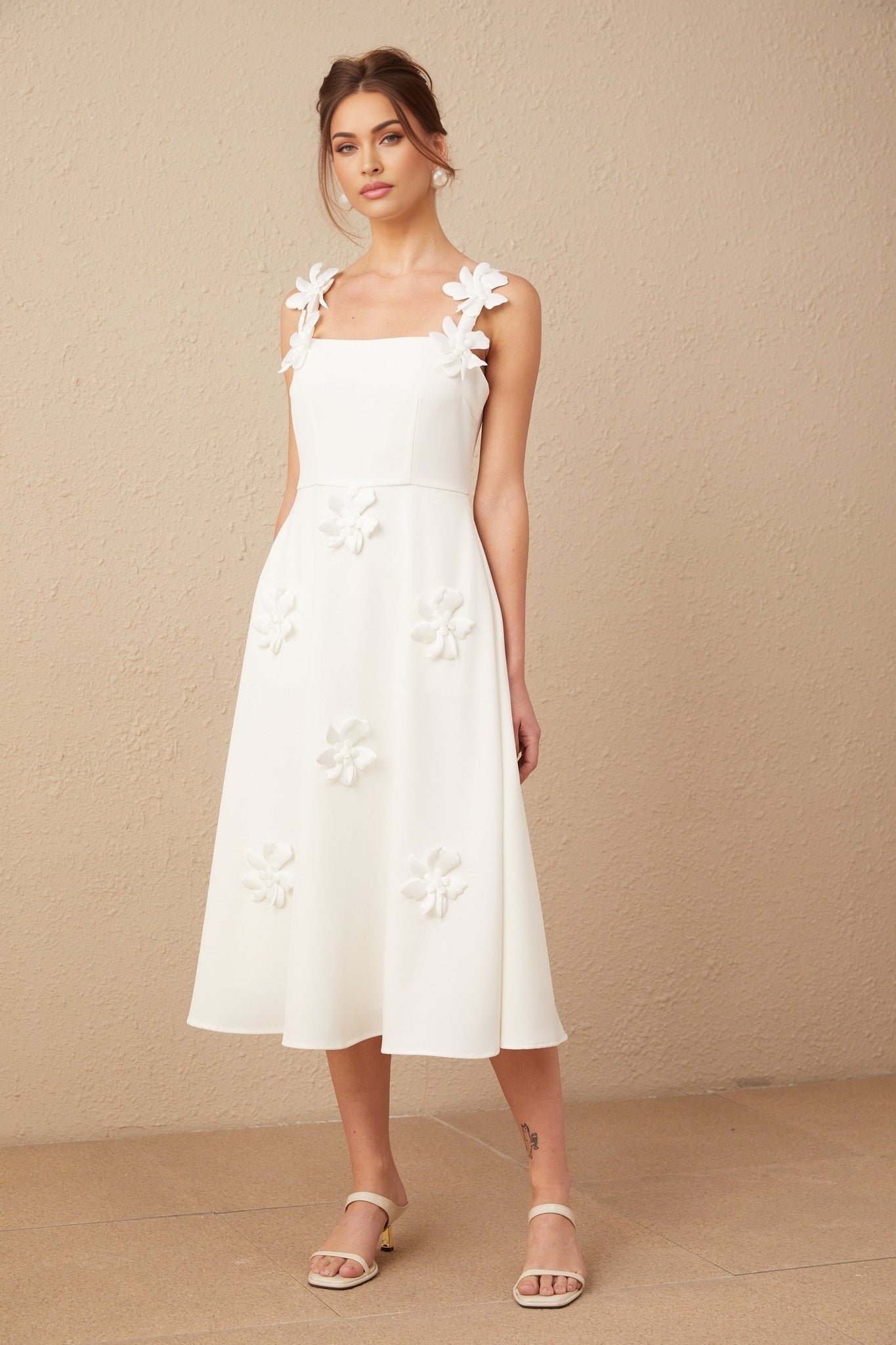 A woman wearing a white midi dress with a square neckline and faux flower details standing in a neutral background