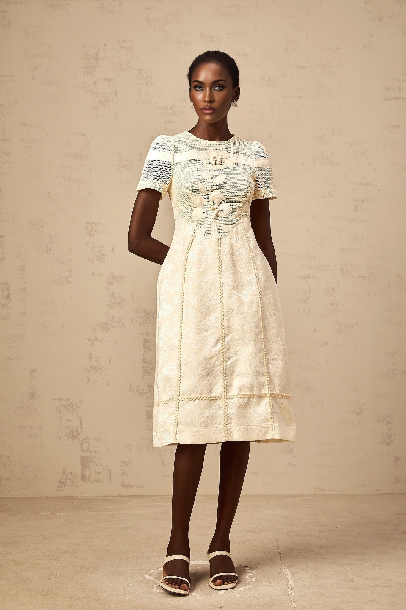 A woman wearing a white midi dress with floral embroidery and openwork details standing in a relaxed pose